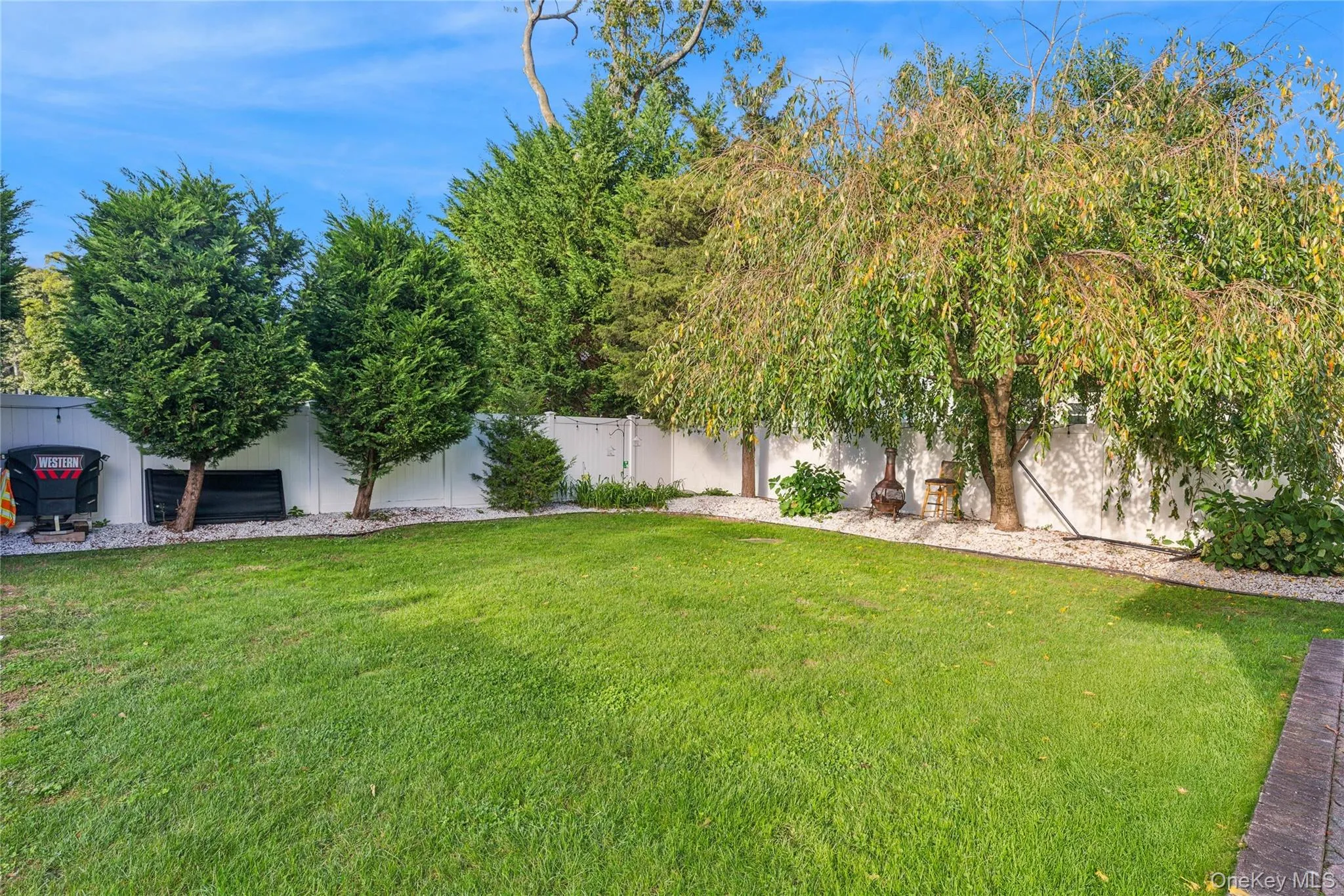 Manicured lawn, white privacy fencing, mature trees, and landscaping with white gravel Manicured lawn, white privacy fencing, mature trees, and landscaping with white gravel