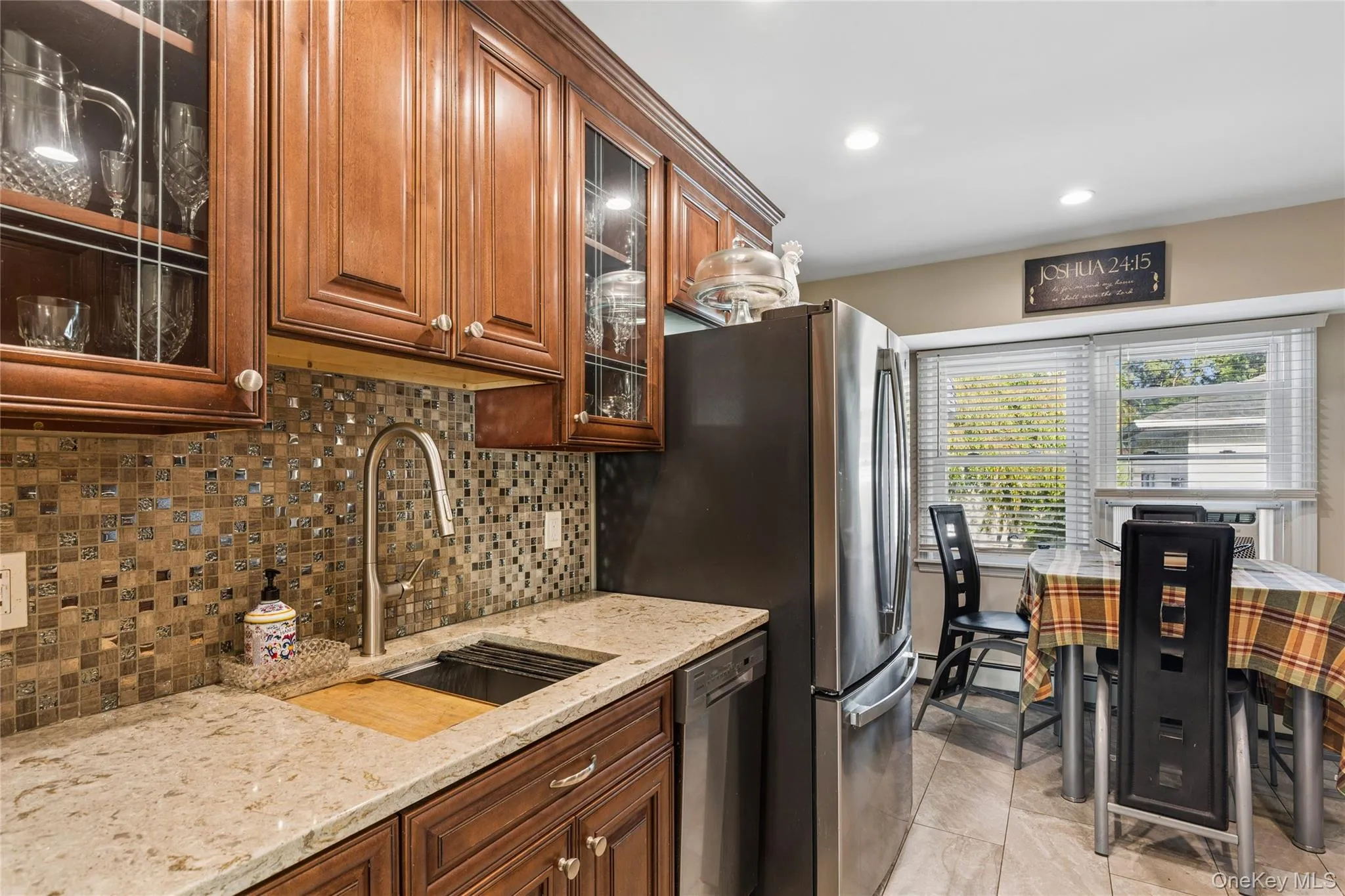 Warm wood cabinetry with glass-front accents, mosaic tile backsplash, integrated stainless steel refrigerator, and recessed lighting Warm wood cabinetry with glass-front accents, mosaic tile backsplash, integrated stainless steel refrigerator, and recessed lighting