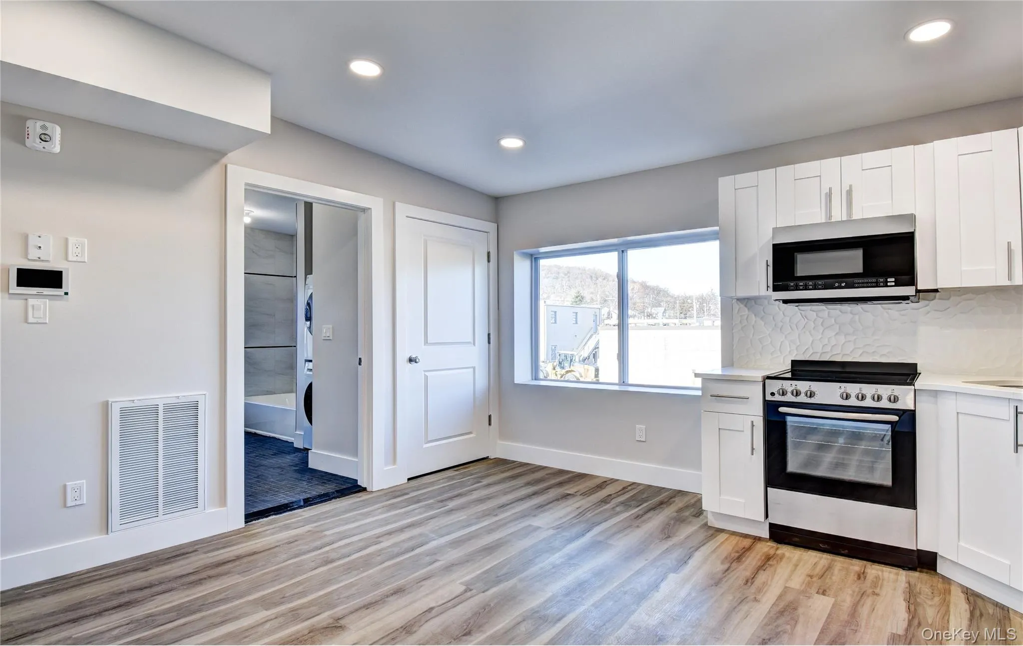 Kitchen with electric stove, stainless steel microwave, white cabinets, recessed lighting, and light wood-type flooring Kitchen with electric stove, stainless steel microwave, white cabinets, recessed lighting, and light wood-type flooring