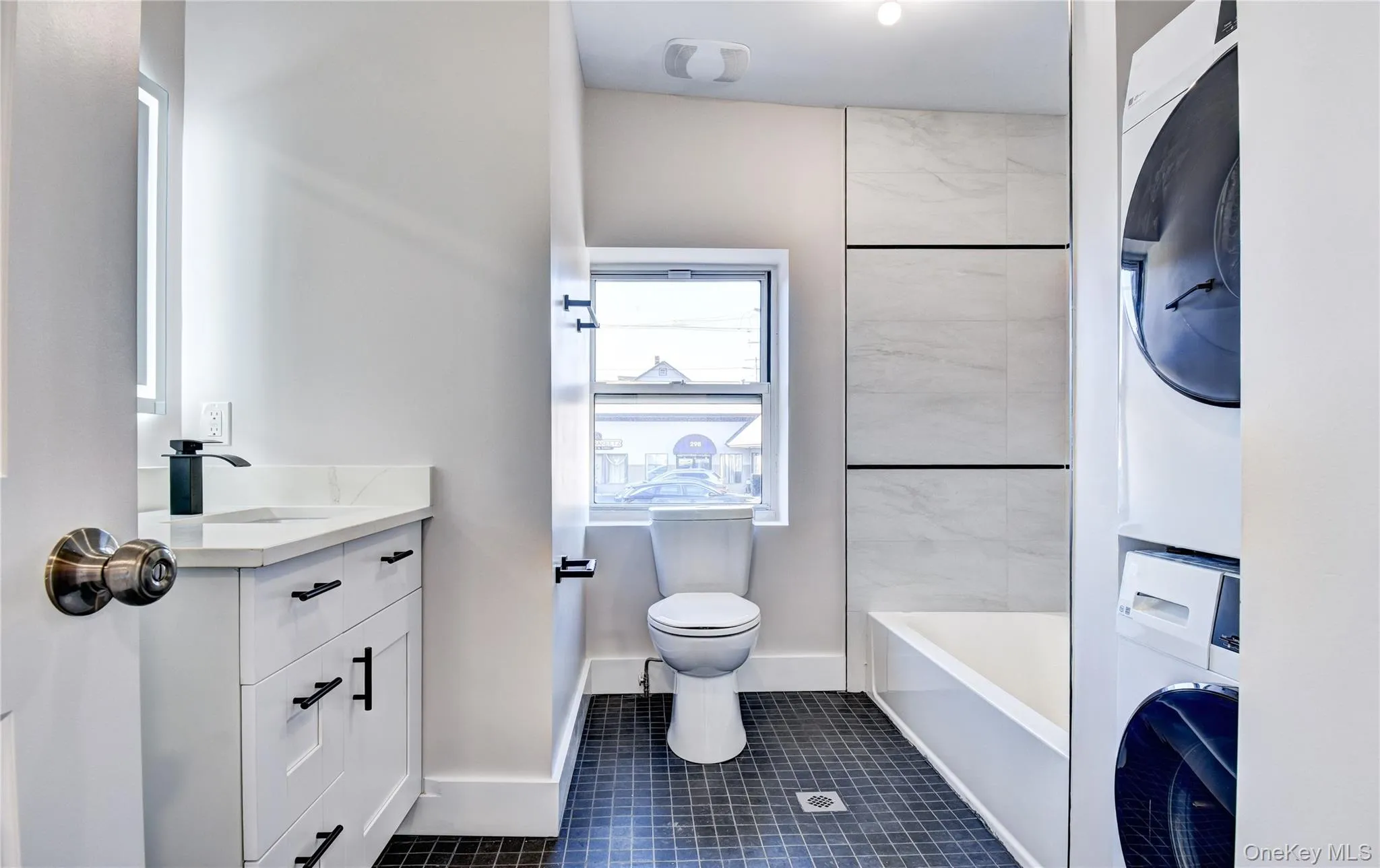 Full bath featuring vanity, dark tile patterned flooring, and stacked washing machine and dryer Full bath featuring vanity, dark tile patterned flooring, and stacked washing machine and dryer