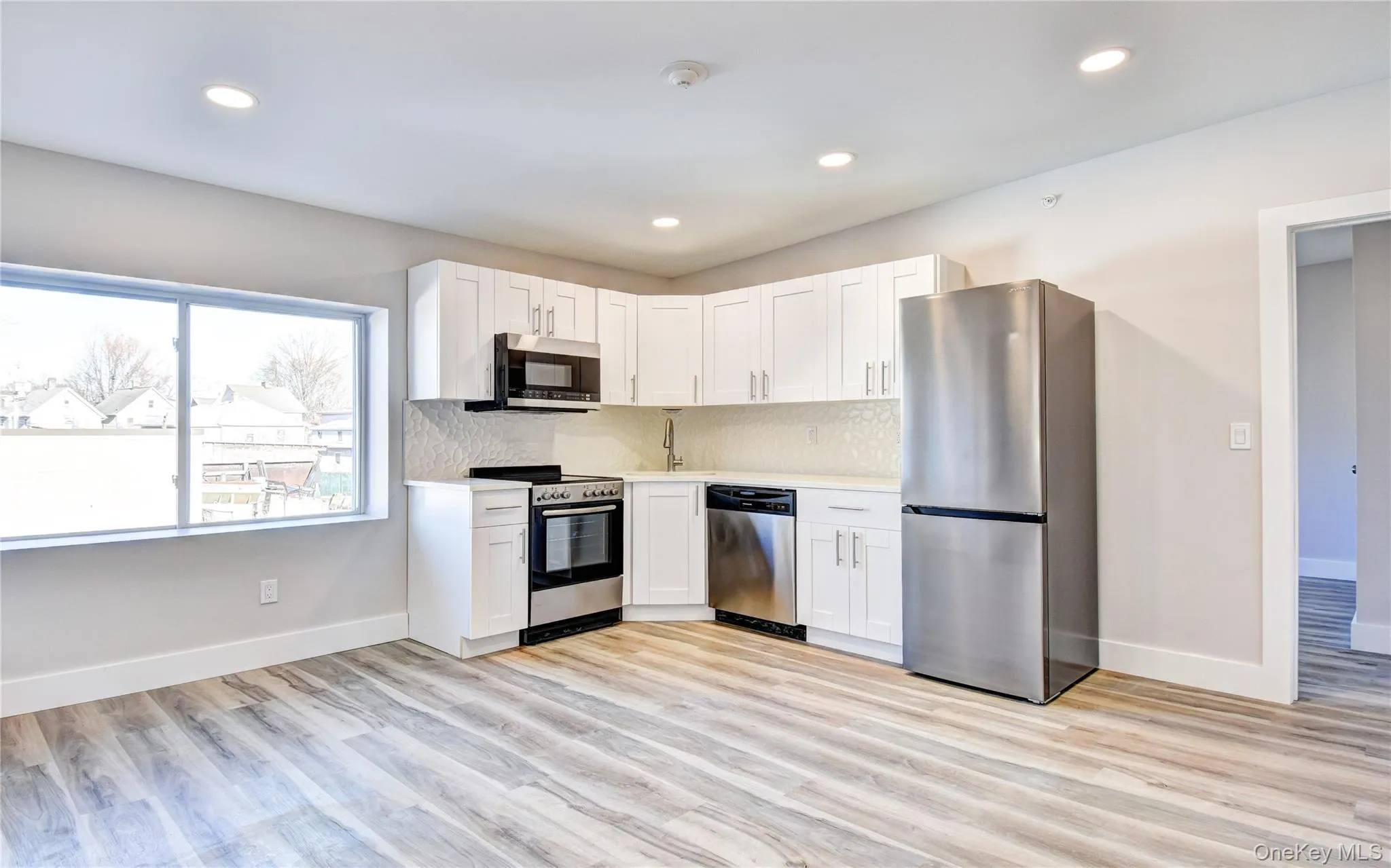 Kitchen with appliances with stainless steel finishes, white cabinetry, light wood-style flooring, backsplash, and recessed lighting Kitchen with appliances with stainless steel finishes, white cabinetry, light wood-style flooring, backsplash, and recessed lighting