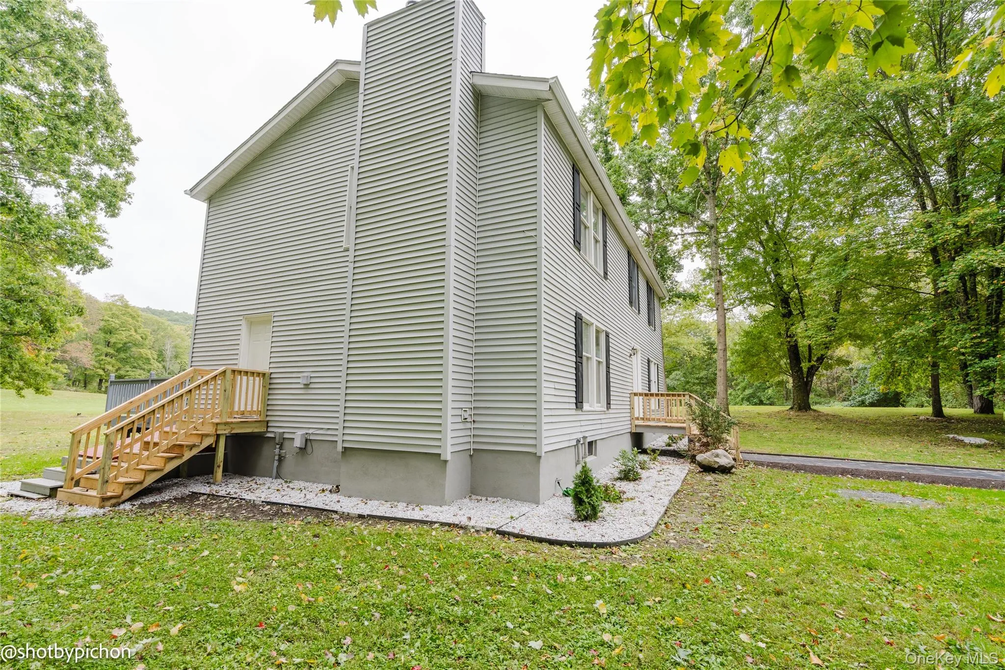 Light-toned siding exterior with a prominent chimney, new wood stairs, and a gravel perimeter Light-toned siding exterior with a prominent chimney, new wood stairs, and a gravel perimeter