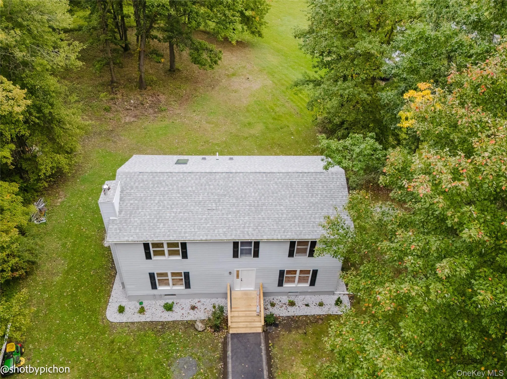 Light gray siding exterior with a new gray shingle roof, contrasting black window shutters, a prominent chimney, and a wooden front deck Light gray siding exterior with a new gray shingle roof, contrasting black window shutters, a prominent chimney, and a wooden front deck