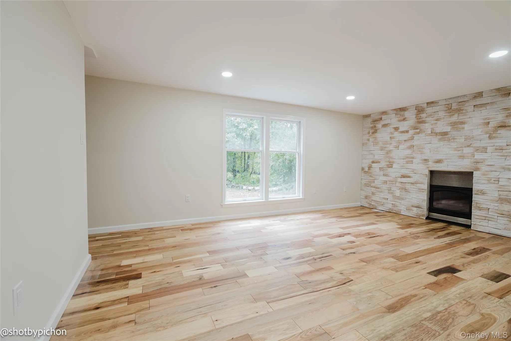 Hardwood flooring, recessed lighting, expansive windows, light-toned walls, and a stone-clad fireplace Hardwood flooring, recessed lighting, expansive windows, light-toned walls, and a stone-clad fireplace