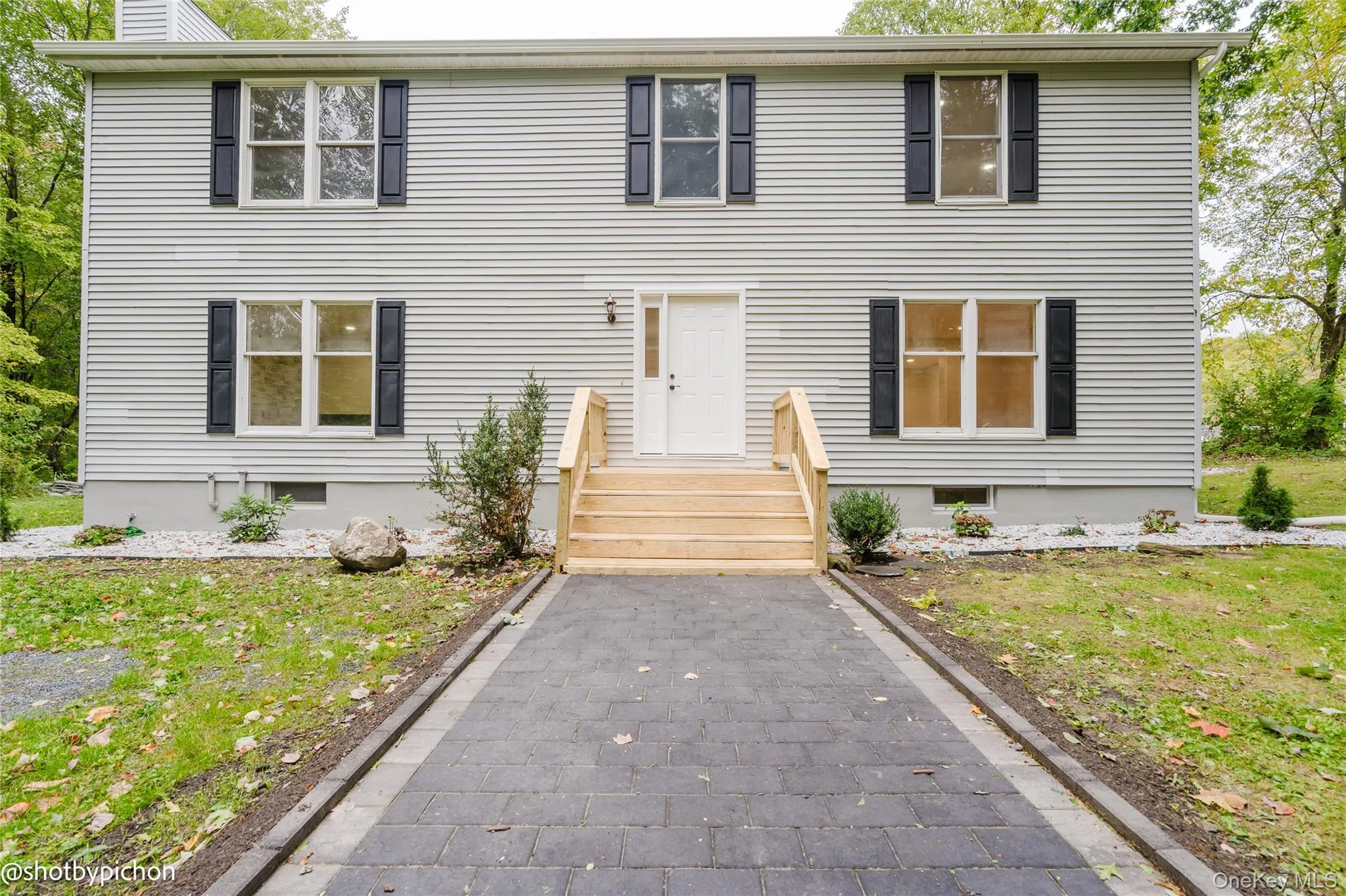 Two-story exterior with horizontal siding, dark window shutters, a paved walkway, and a landscaped entry with wooden steps Two-story exterior with horizontal siding, dark window shutters, a paved walkway, and a landscaped entry with wooden steps