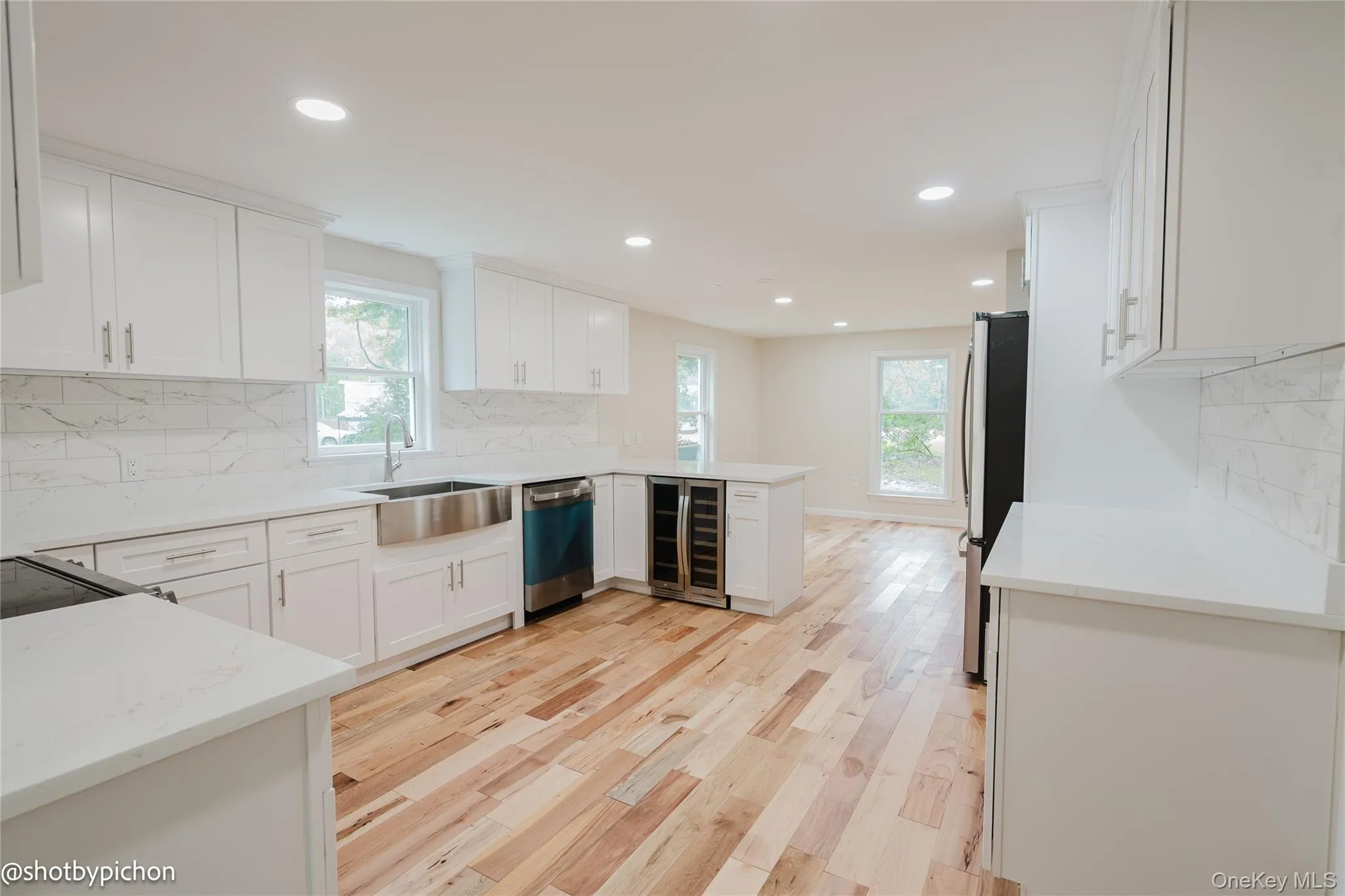 Kitchen featuring white cabinetry, light-toned wood flooring, stainless steel farmhouse sink, integrated wine refrigerator, and recessed lighting Kitchen featuring white cabinetry, light-toned wood flooring, stainless steel farmhouse sink, integrated wine refrigerator, and recessed lighting