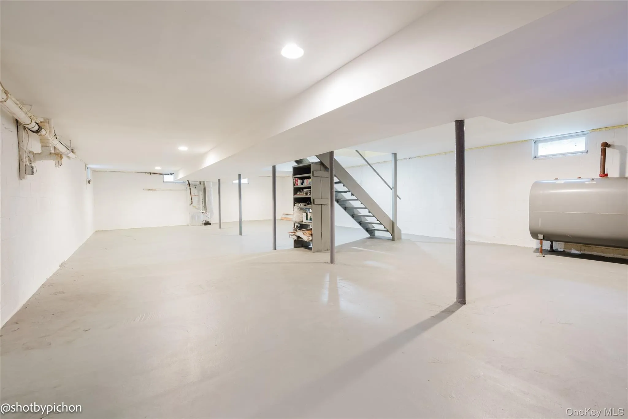 Expansive open space featuring recessed lighting, a painted concrete floor, and a metal staircase Expansive open space featuring recessed lighting, a painted concrete floor, and a metal staircase