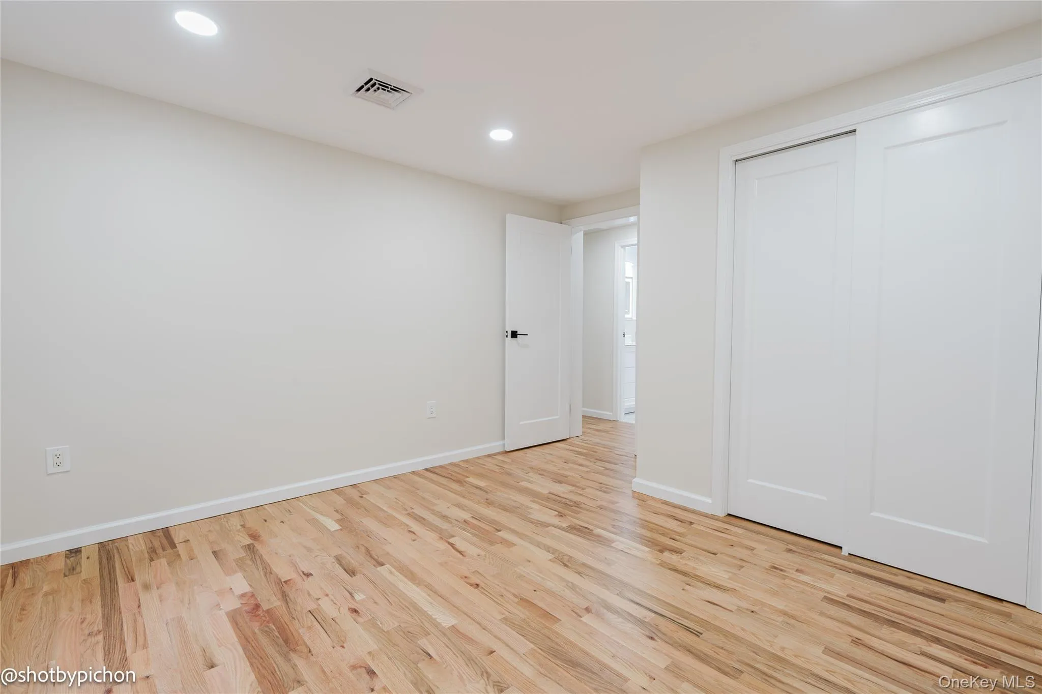 Wood-finish flooring with recessed lighting, white walls, and white sliding closet doors Wood-finish flooring with recessed lighting, white walls, and white sliding closet doors