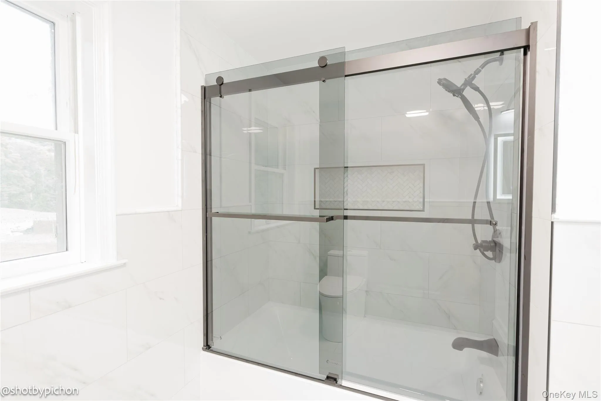Sliding glass shower enclosure with dark bronze hardware, a recessed tile niche, and a wall-mounted showerhead Sliding glass shower enclosure with dark bronze hardware, a recessed tile niche, and a wall-mounted showerhead