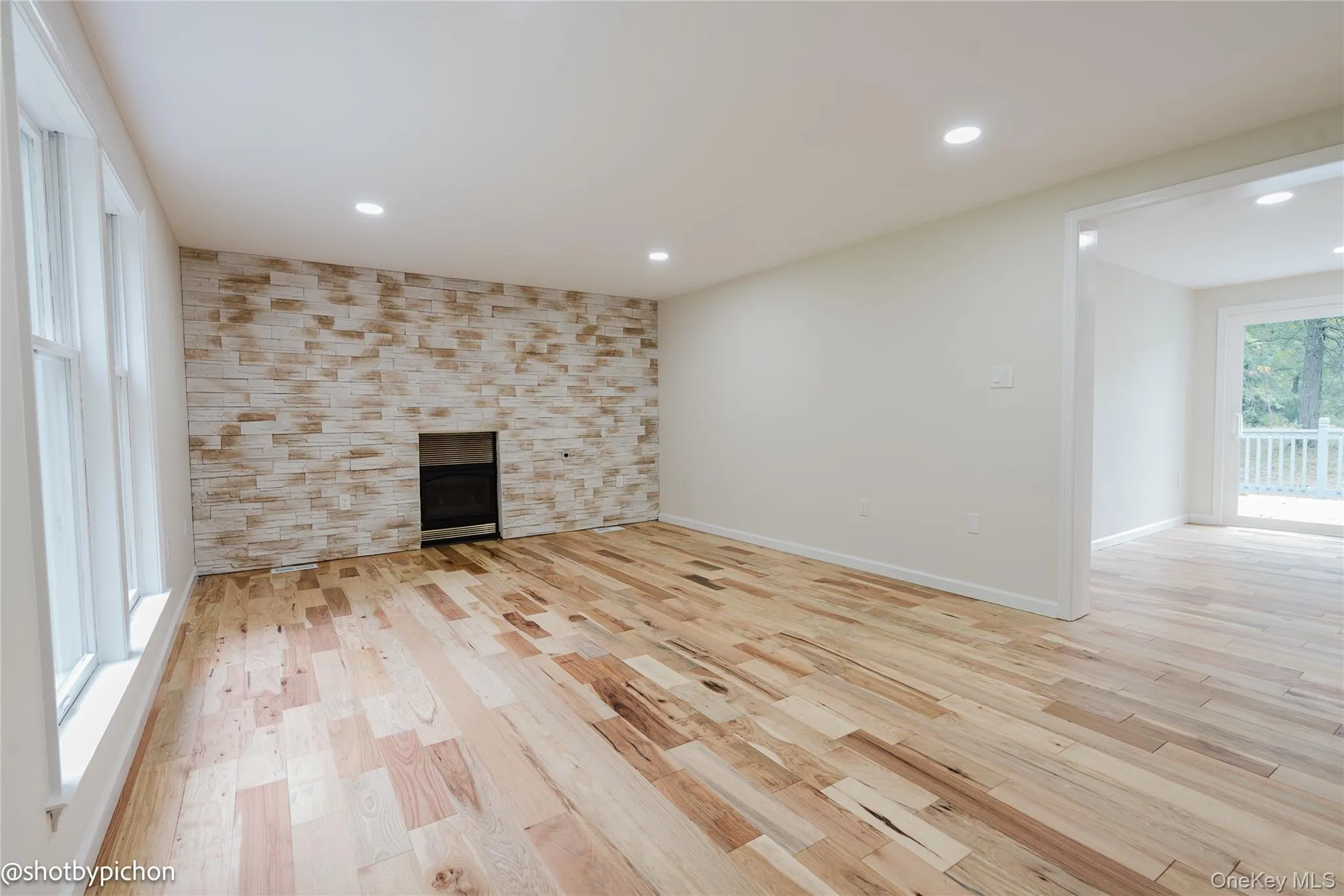 Hardwood flooring, recessed lighting, expansive windows, stacked stone fireplace surround, and a sliding glass door to an outdoor deck Hardwood flooring, recessed lighting, expansive windows, stacked stone fireplace surround, and a sliding glass door to an outdoor deck