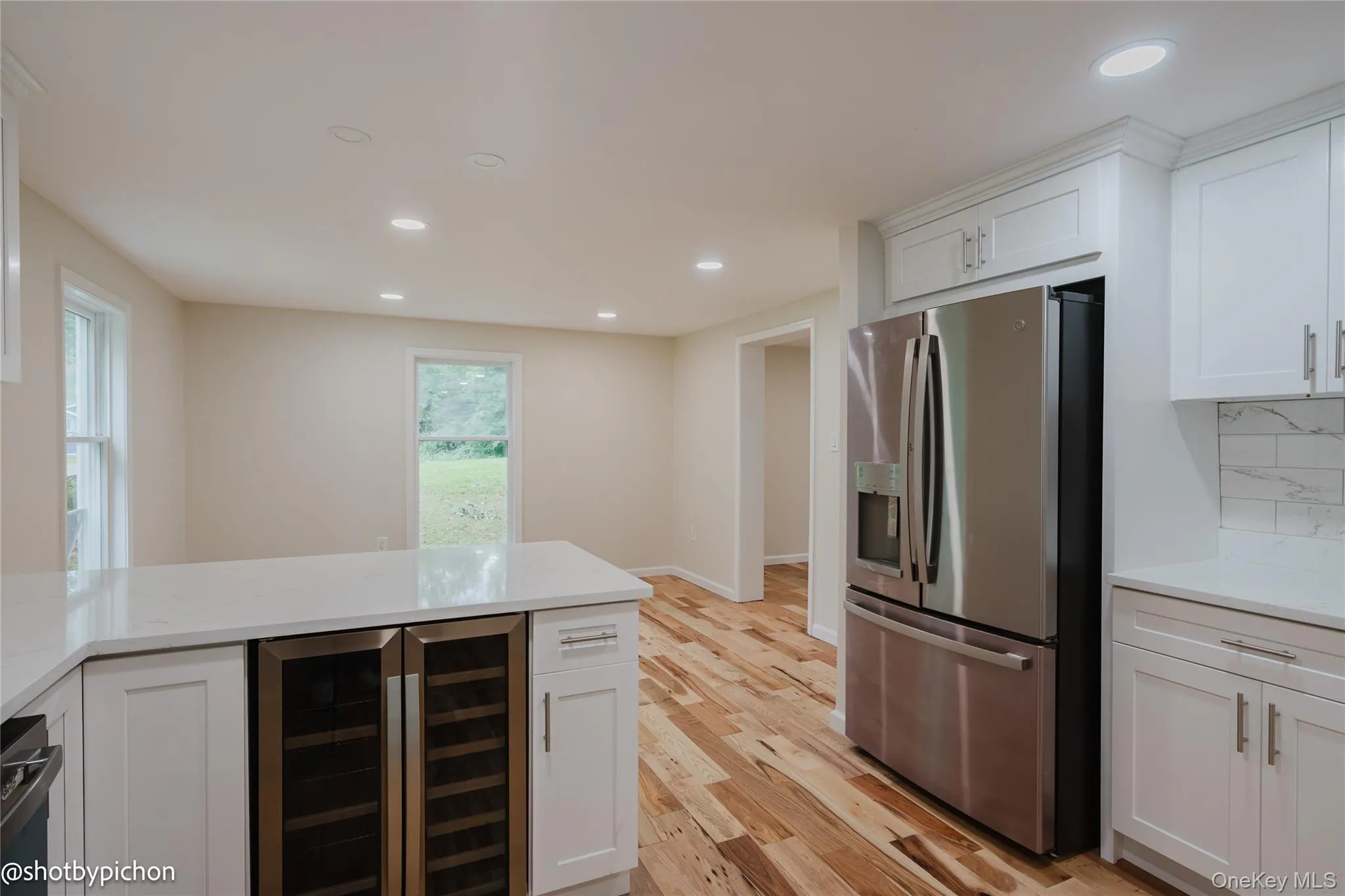 White shaker cabinetry, stainless steel refrigerator, white countertops, wood-finish flooring, and recessed lighting White shaker cabinetry, stainless steel refrigerator, white countertops, wood-finish flooring, and recessed lighting