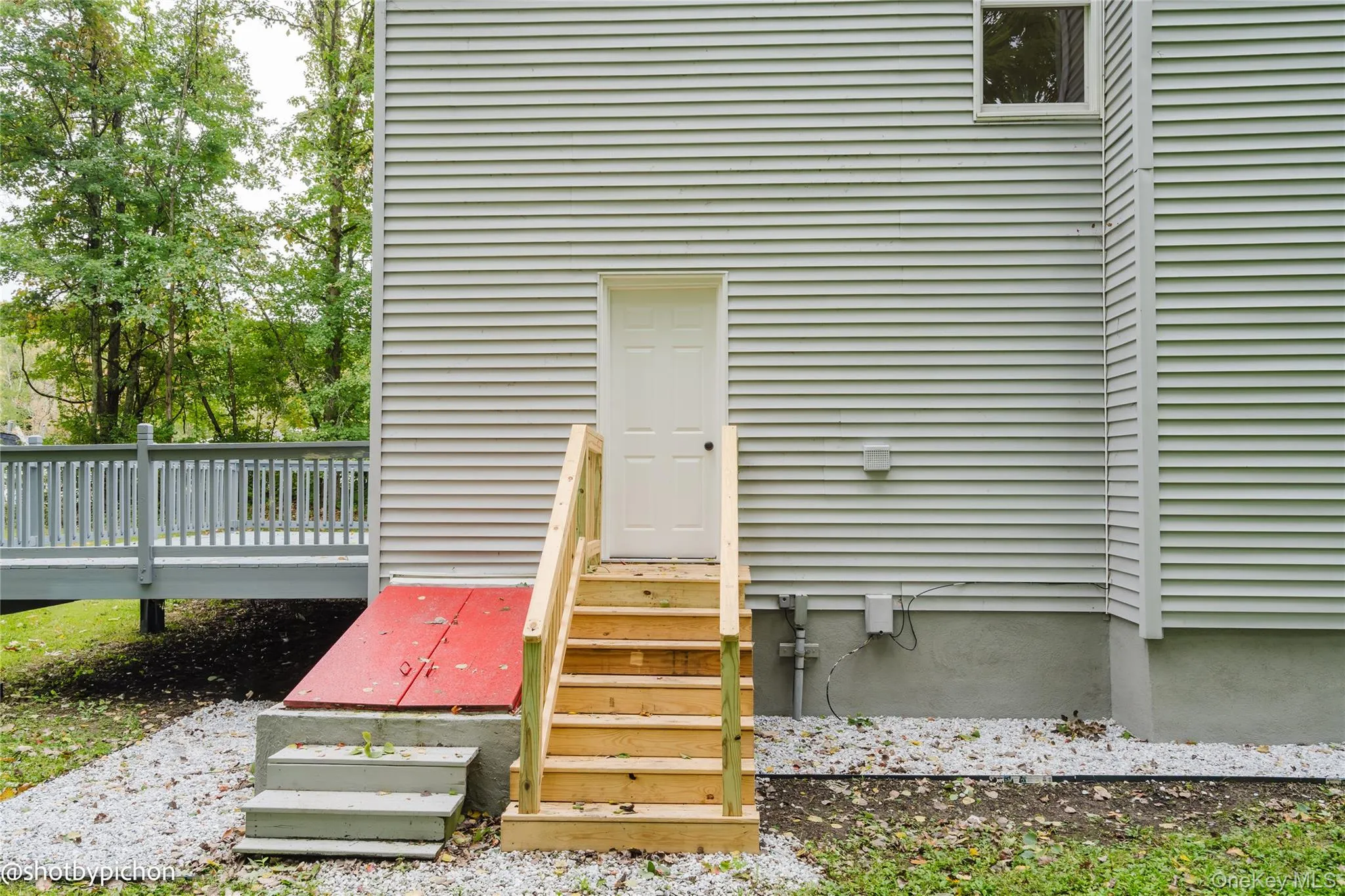Light gray siding exterior with a white door and wood stairs Light gray siding exterior with a white door and wood stairs