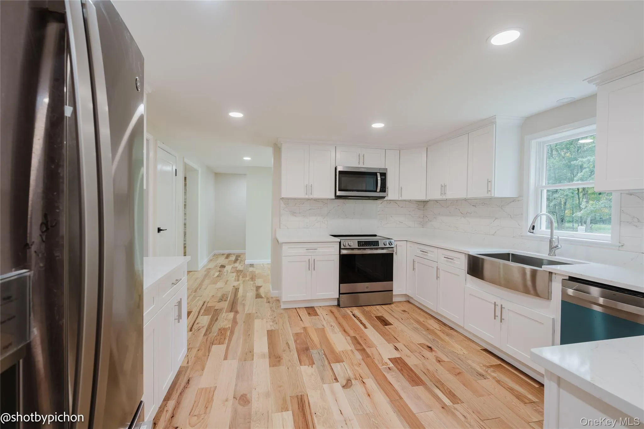 Kitchen featuring white cabinetry, stainless steel appliances, wood-finish flooring, a stainless steel apron sink, and recessed lighting Kitchen featuring white cabinetry, stainless steel appliances, wood-finish flooring, a stainless steel apron sink, and recessed lighting