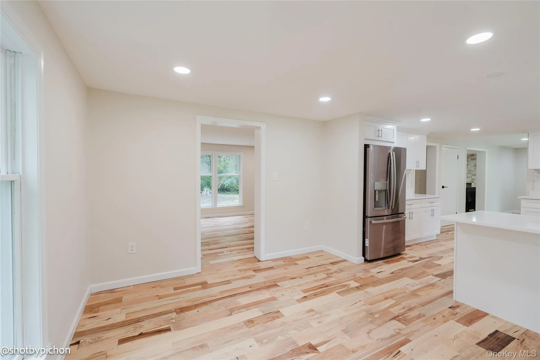 Wood-finish flooring throughout, recessed lighting, white cabinetry, stainless steel refrigerator, and white countertops Wood-finish flooring throughout, recessed lighting, white cabinetry, stainless steel refrigerator, and white countertops