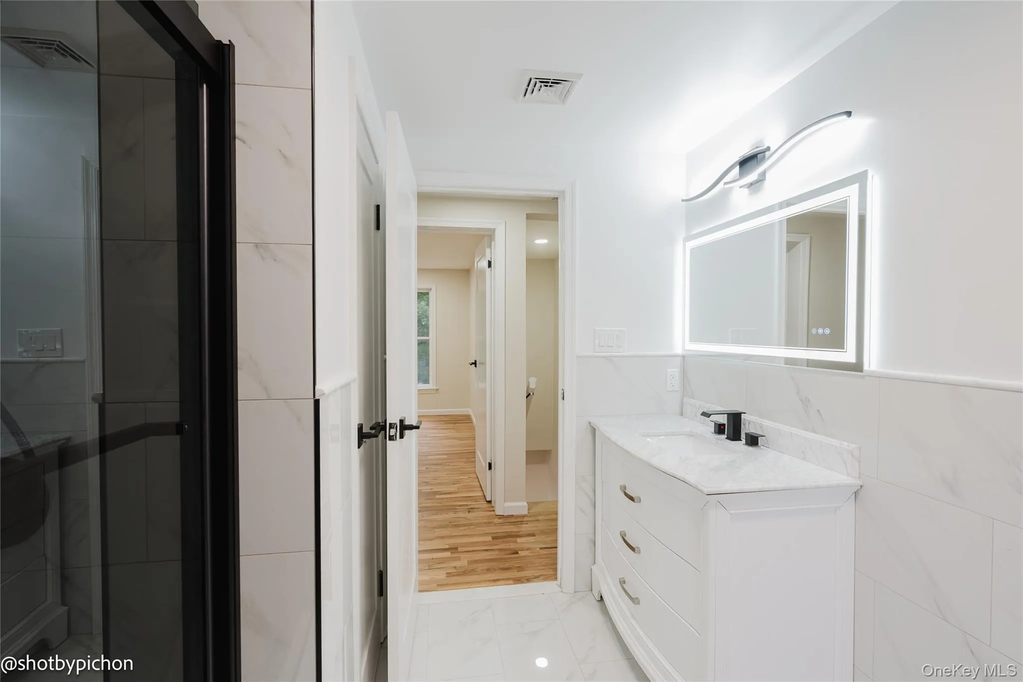 Bathroom featuring a single vanity with a white countertop, a rectangular LED-backlit mirror, and a wall-mounted light fixture Bathroom featuring a single vanity with a white countertop, a rectangular LED-backlit mirror, and a wall-mounted light fixture