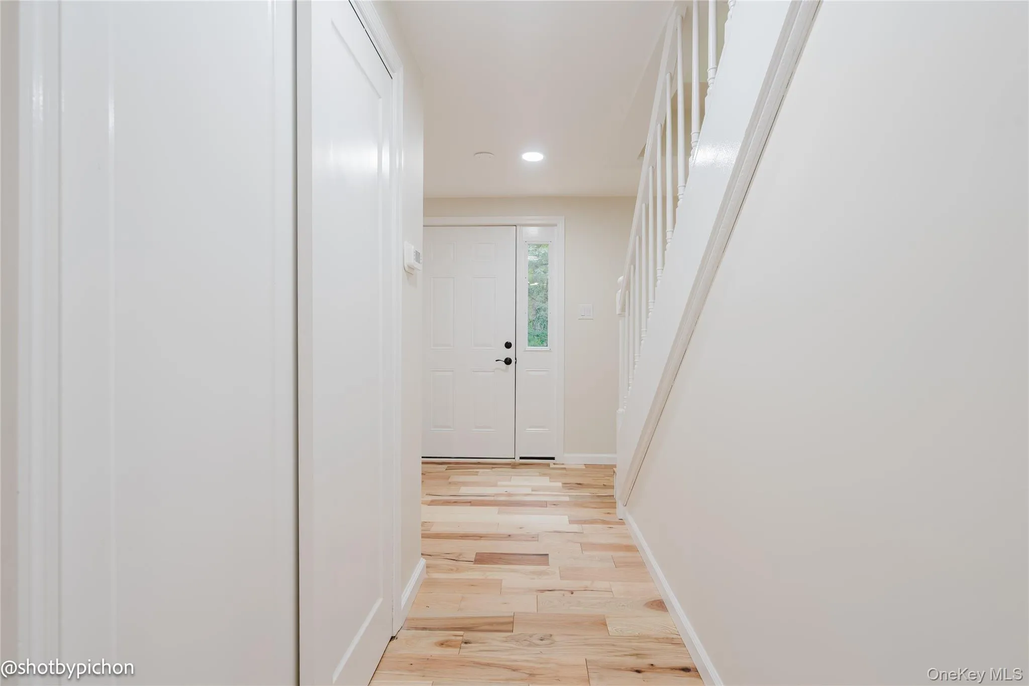Entryway featuring wood-finish flooring, white panel doors, recessed lighting, and a white staircase with balusters Entryway featuring wood-finish flooring, white panel doors, recessed lighting, and a white staircase with balusters