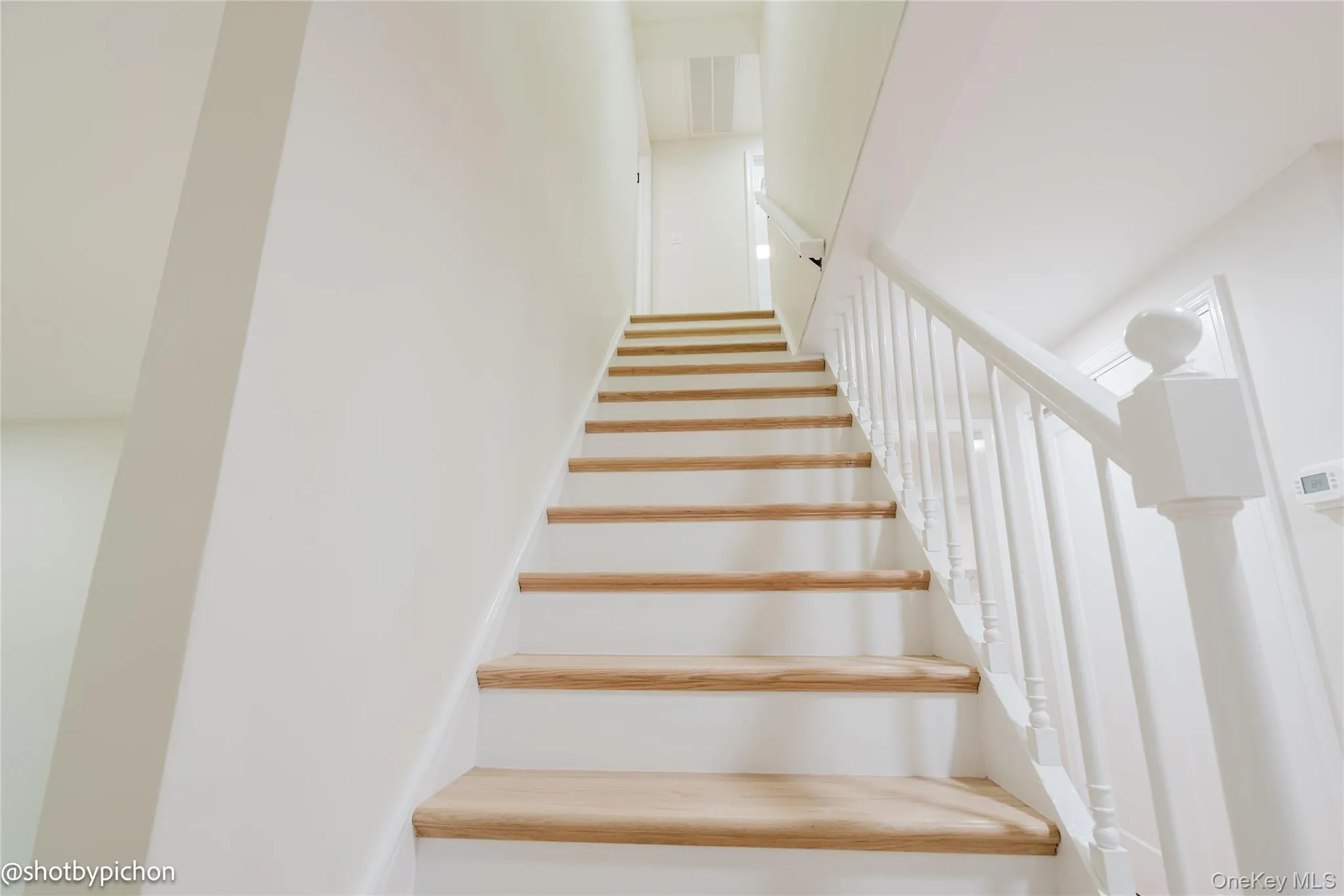 Staircase with wood-finish treads and white risers, featuring a white baluster railing system Staircase with wood-finish treads and white risers, featuring a white baluster railing system