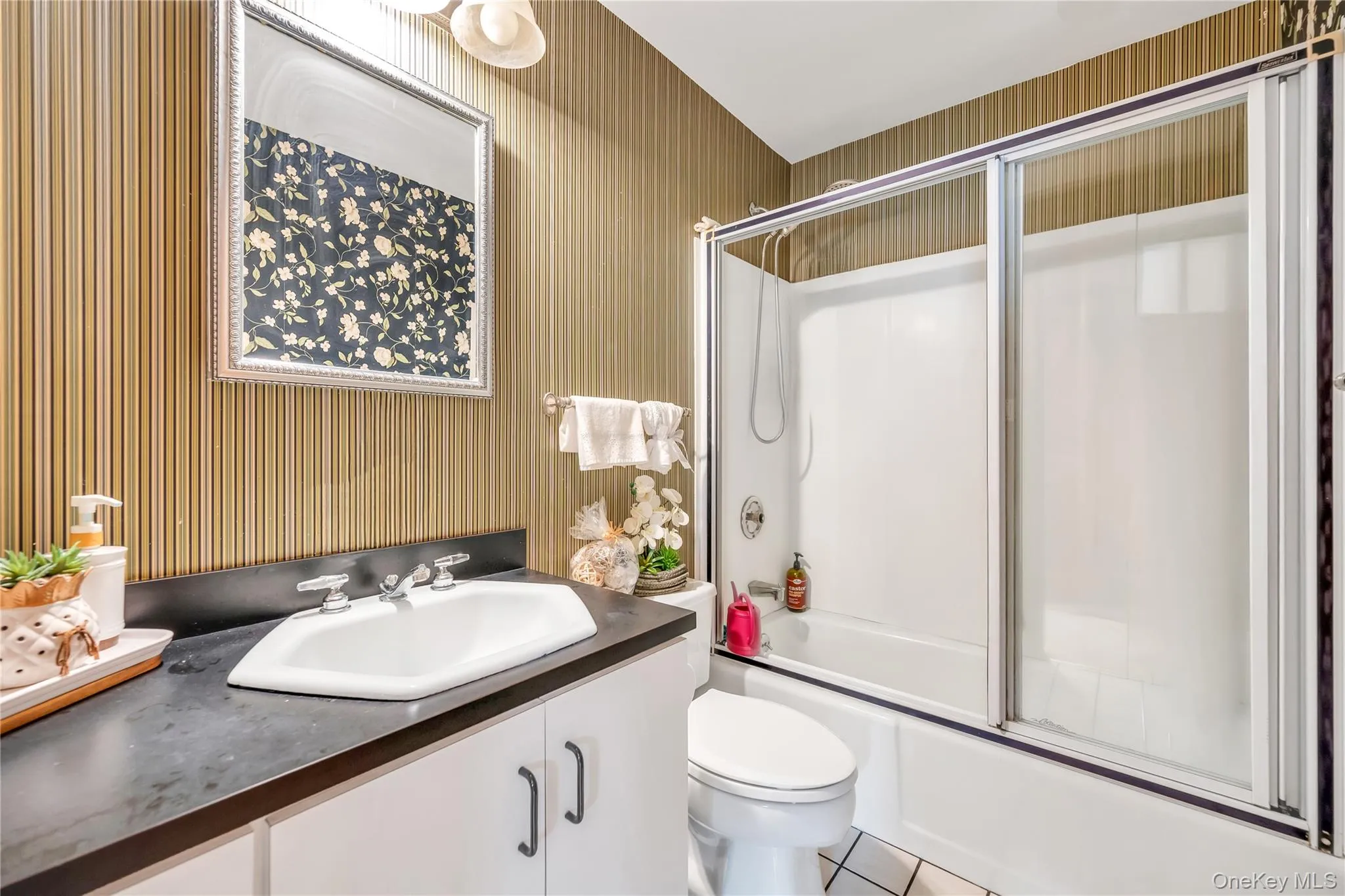 Full bath with wallpapered walls, vanity, combined bath / shower with glass door, and tile patterned flooring Full bath with wallpapered walls, vanity, combined bath / shower with glass door, and tile patterned flooring