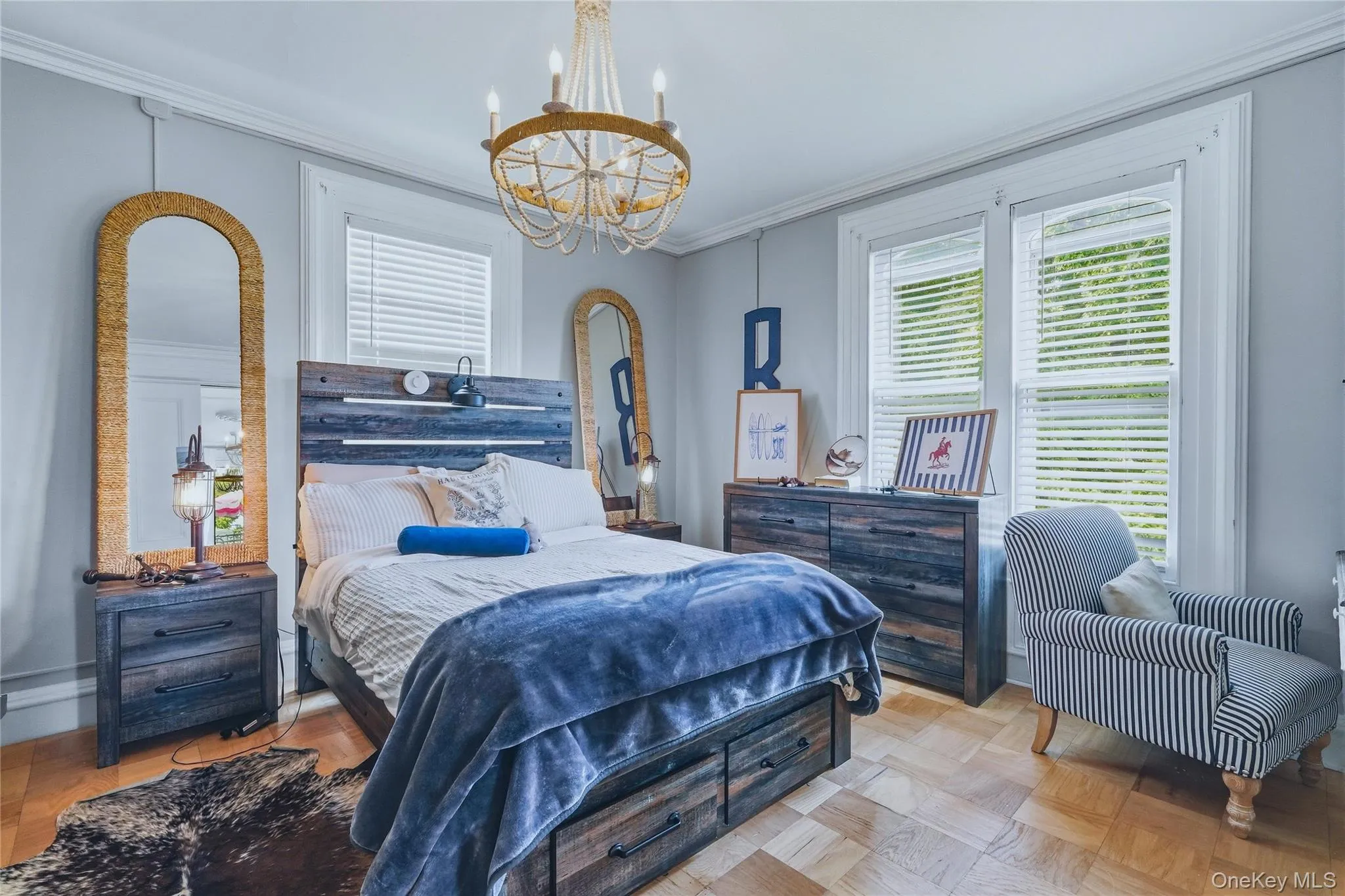 Light-colored wood-finish flooring, two large windows with blinds, crown molding, and a decorative chandelier Light-colored wood-finish flooring, two large windows with blinds, crown molding, and a decorative chandelier