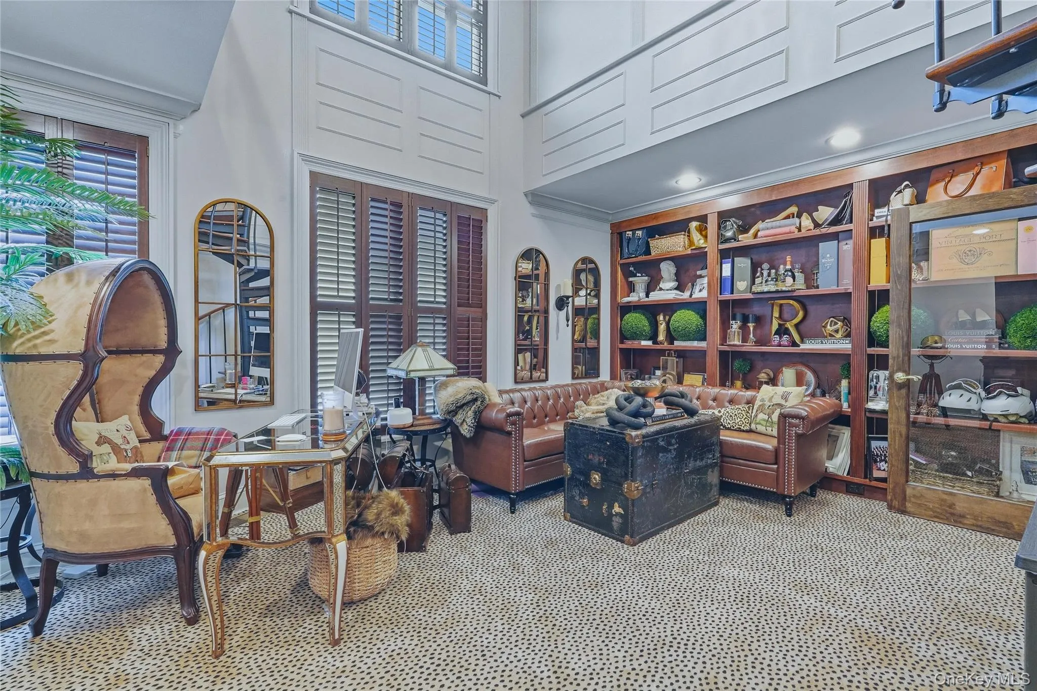 Two-story room featuring extensive built-in wooden shelving, dark wood plantation shutters, and a spiral staircase Two-story room featuring extensive built-in wooden shelving, dark wood plantation shutters, and a spiral staircase