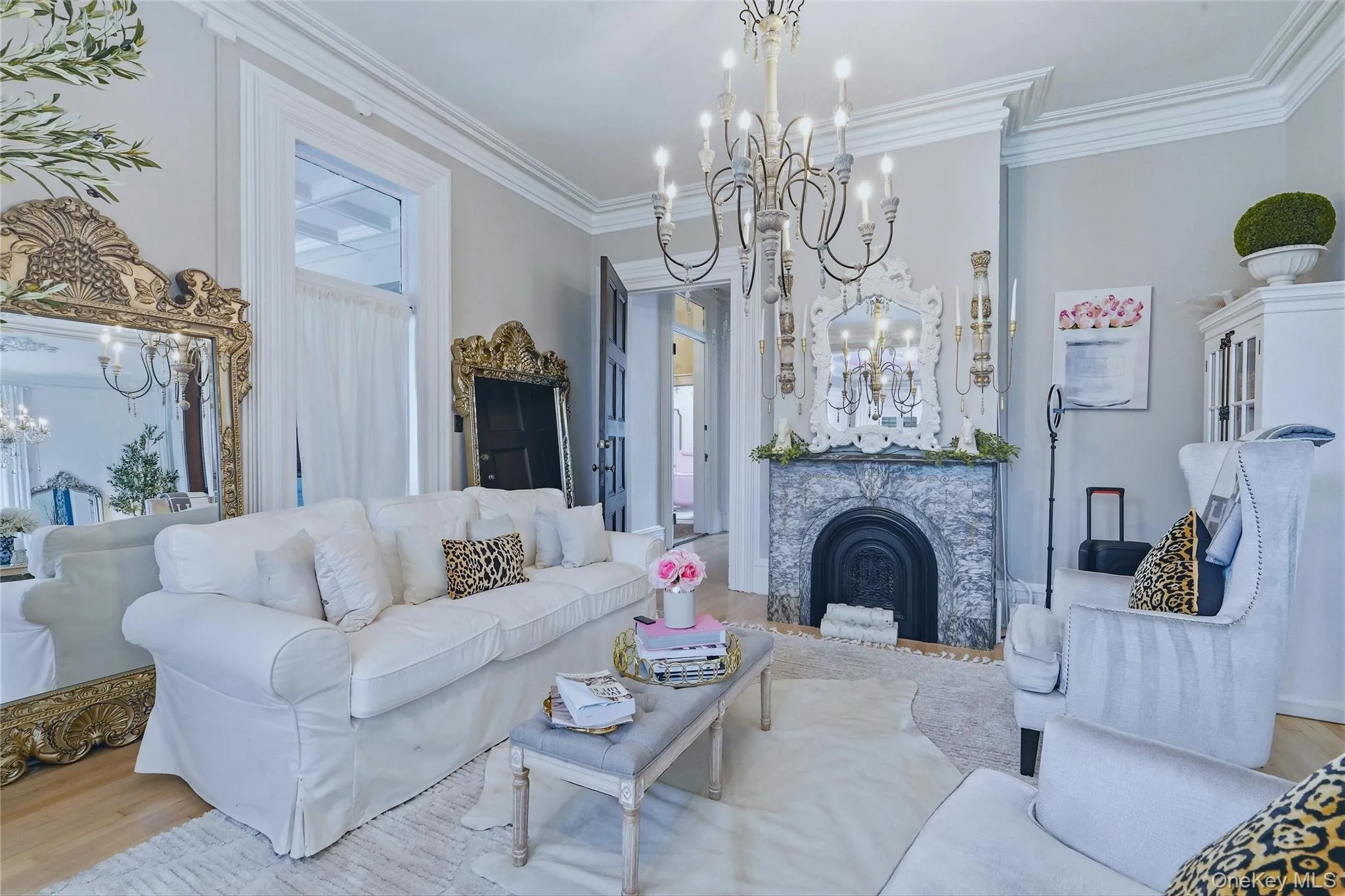 Ornate chandelier, decorative fireplace with stone surround, crown molding, and light wood-finish flooring Ornate chandelier, decorative fireplace with stone surround, crown molding, and light wood-finish flooring