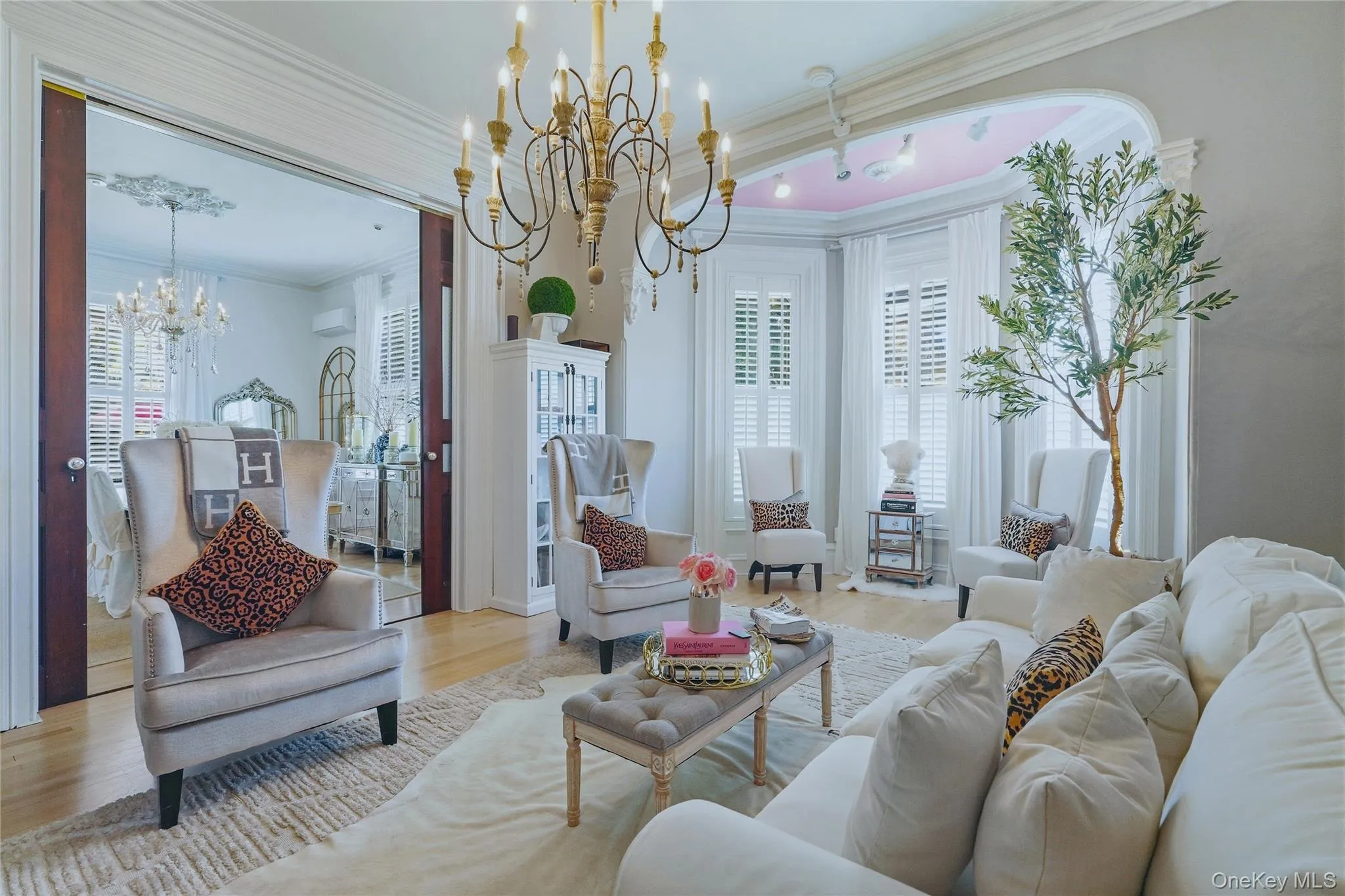 Hardwood flooring, ornate crown molding, decorative chandelier, bay window with plantation shutters, and an arched entry Hardwood flooring, ornate crown molding, decorative chandelier, bay window with plantation shutters, and an arched entry