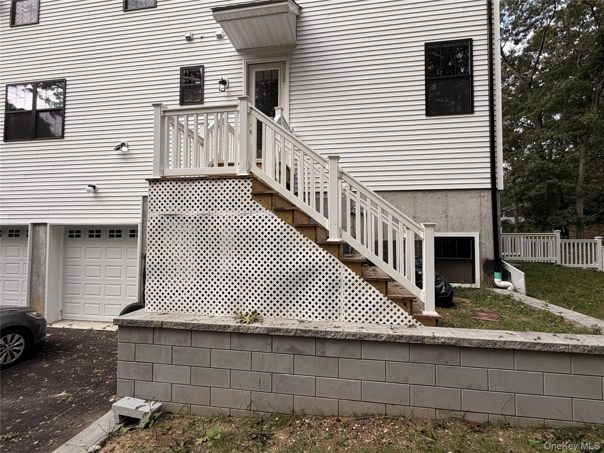 White vinyl siding exterior with two garage bays, an exterior staircase with white railings, and a retaining wall White vinyl siding exterior with two garage bays, an exterior staircase with white railings, and a retaining wall