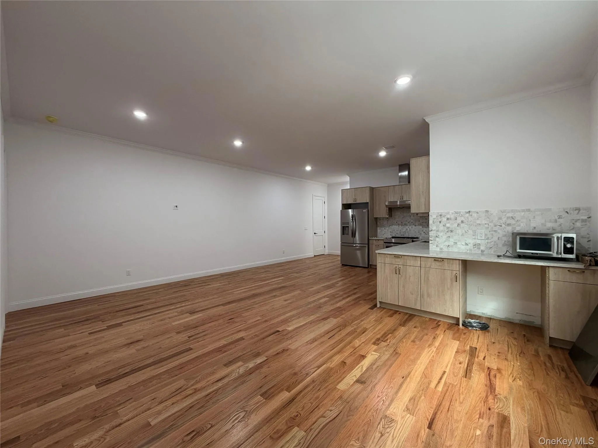 Wood-finish flooring throughout, recessed lighting, crown molding, kitchen with stainless steel appliances, and a tiled backsplash Wood-finish flooring throughout, recessed lighting, crown molding, kitchen with stainless steel appliances, and a tiled backsplash