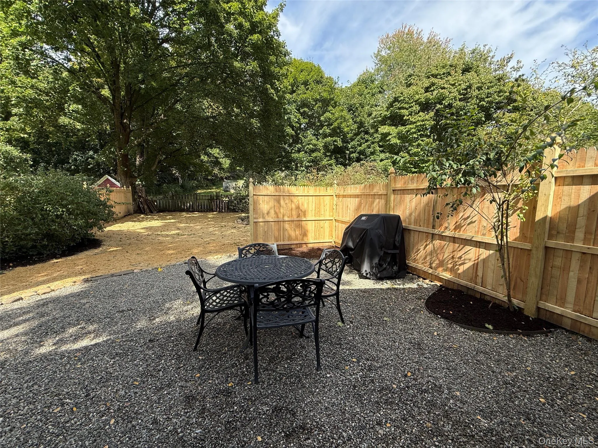 Back yard with gravel seating area and privacy fence. Beyond is newly planted grass about to sprout. Back yard with gravel seating area and privacy fence. Beyond is newly planted grass about to sprout.