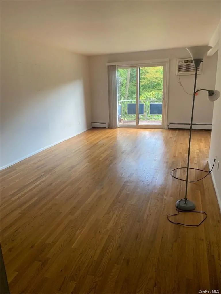 Spacious living room with oak floors and sliders to a deck overlooking a grassy treed area Spacious living room with oak floors and sliders to a deck overlooking a grassy treed area