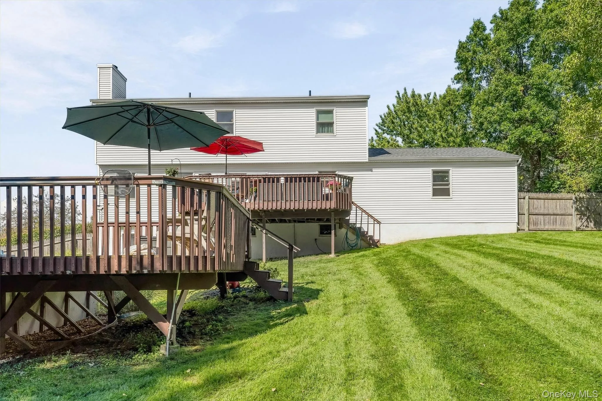 Multi-level wood deck with railings and steps, leading to a sloped grassy yard Multi-level wood deck with railings and steps, leading to a sloped grassy yard