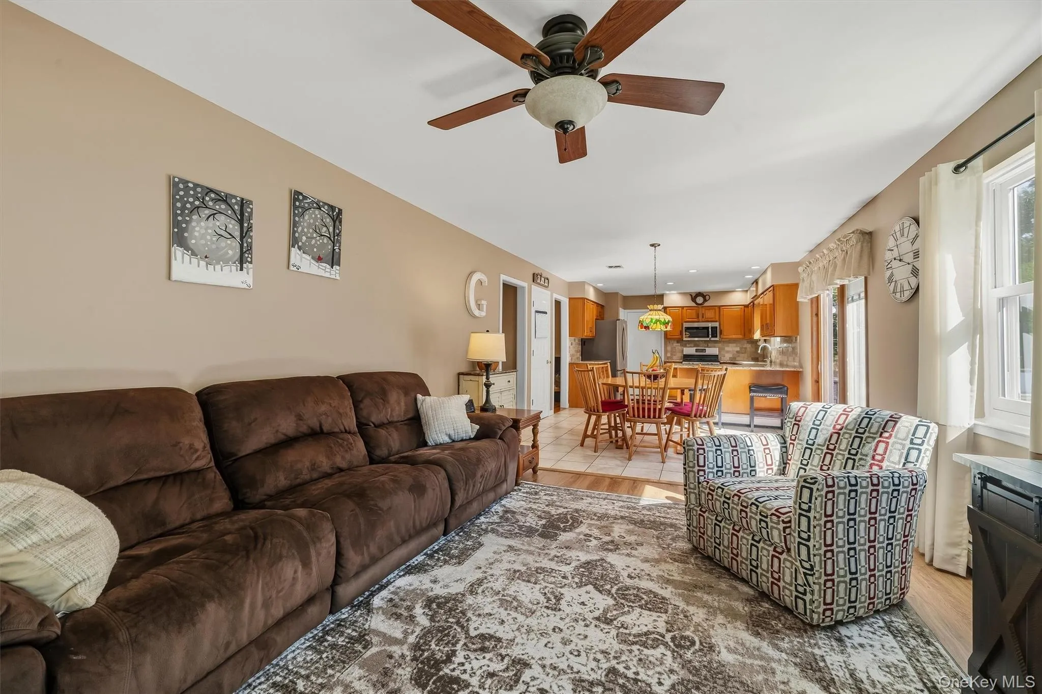 Spacious living area with ceiling fan and wood-finish flooring extending into the kitchen Spacious living area with ceiling fan and wood-finish flooring extending into the kitchen