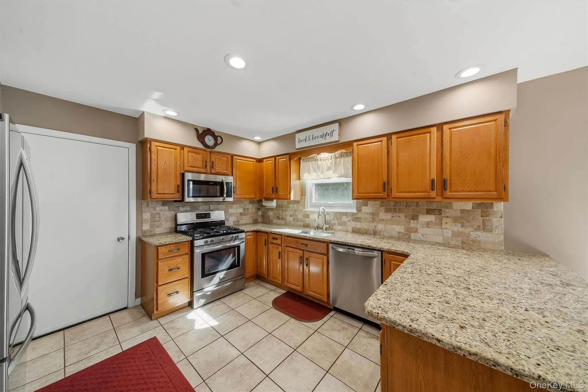 Kitchen featuring tile flooring, wood-finish cabinetry, stone countertops, and stainless steel appliances Kitchen featuring tile flooring, wood-finish cabinetry, stone countertops, and stainless steel appliances