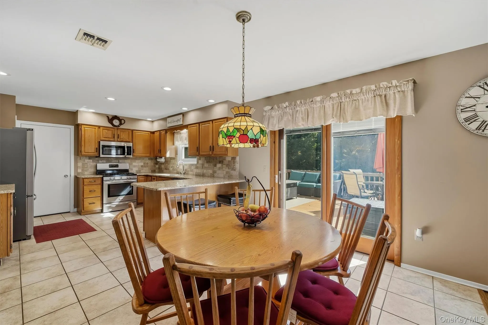 Kitchen featuring wood-finish cabinetry, tile flooring, stainless steel appliances, and a peninsula with countertop seating Kitchen featuring wood-finish cabinetry, tile flooring, stainless steel appliances, and a peninsula with countertop seating