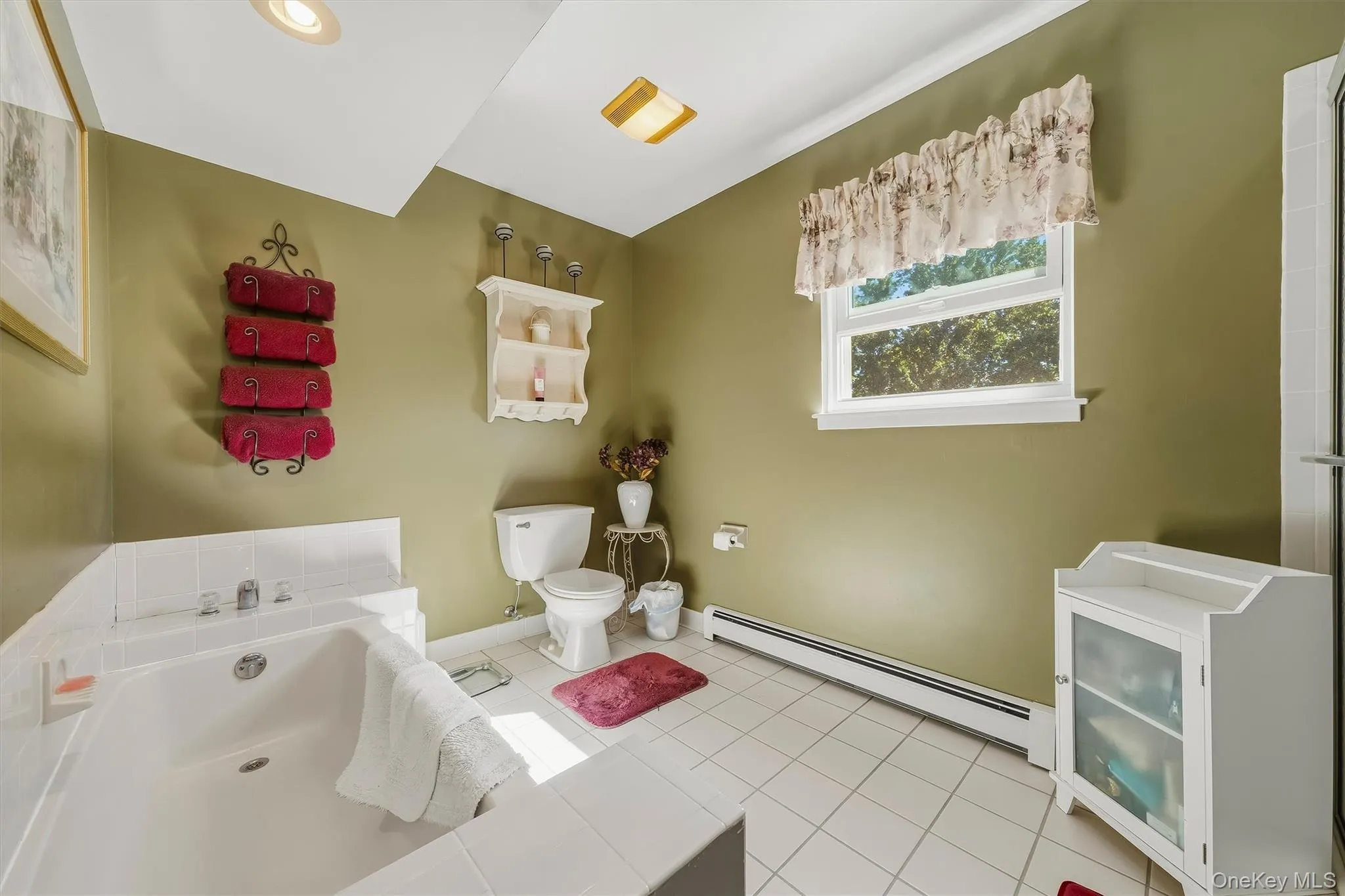 White tile flooring, built-in soaking tub, single window, recessed ceiling lighting, and a white toilet White tile flooring, built-in soaking tub, single window, recessed ceiling lighting, and a white toilet