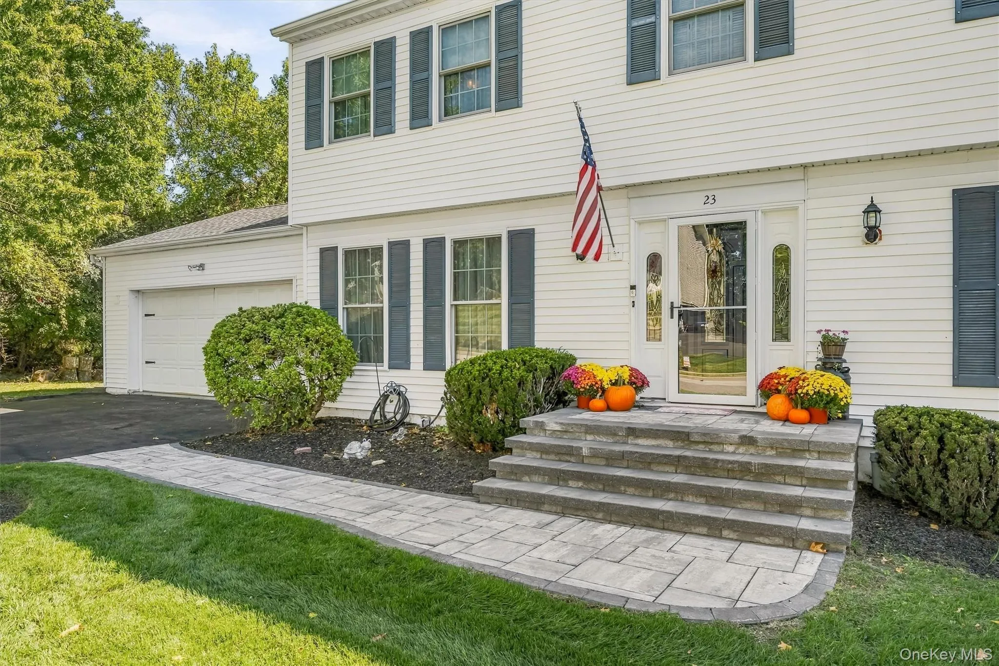 Welcoming front elevation featuring a two-story Colonial design with white horizontal siding, multi-pane windows, and a covered entry portico with stone steps Welcoming front elevation featuring a two-story Colonial design with white horizontal siding, multi-pane windows, and a covered entry portico with stone steps
