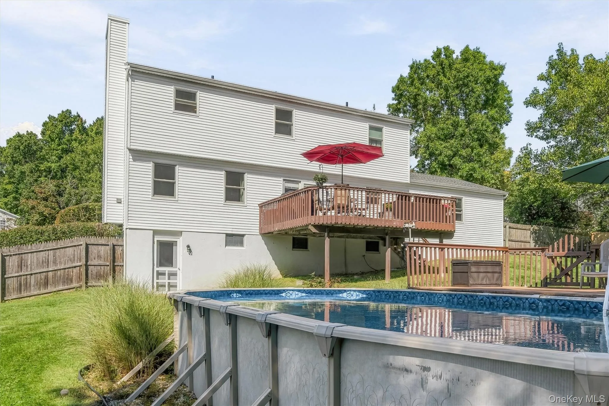 Two-story exterior with white siding, elevated wood deck with railing, ground-level screened door, and an above-ground swimming pool Two-story exterior with white siding, elevated wood deck with railing, ground-level screened door, and an above-ground swimming pool