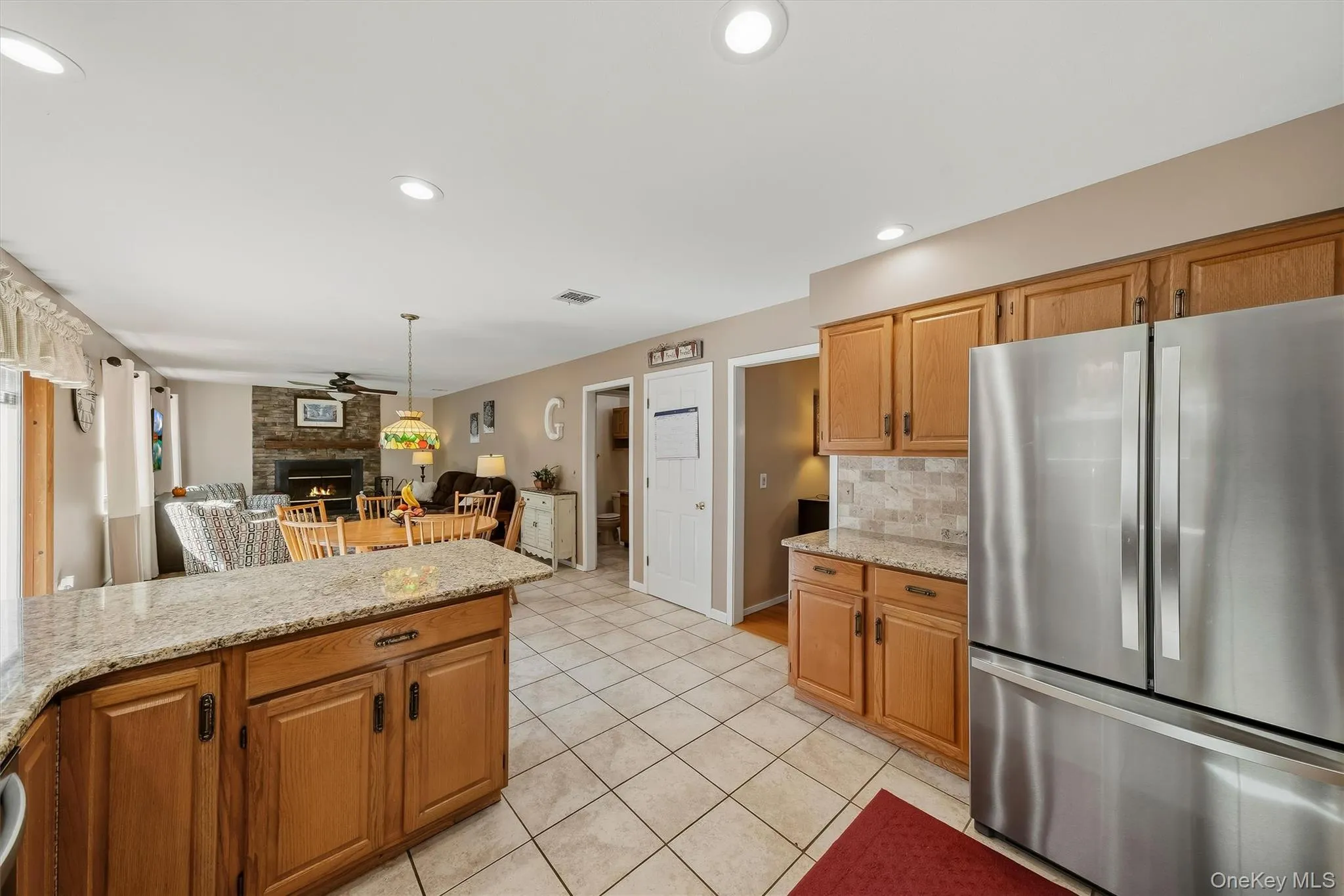 Spacious kitchen featuring warm wood cabinetry, granite countertops, stainless steel appliances including side-by-side refrigerator, and a large center island with seating Spacious kitchen featuring warm wood cabinetry, granite countertops, stainless steel appliances including side-by-side refrigerator, and a large center island with seating