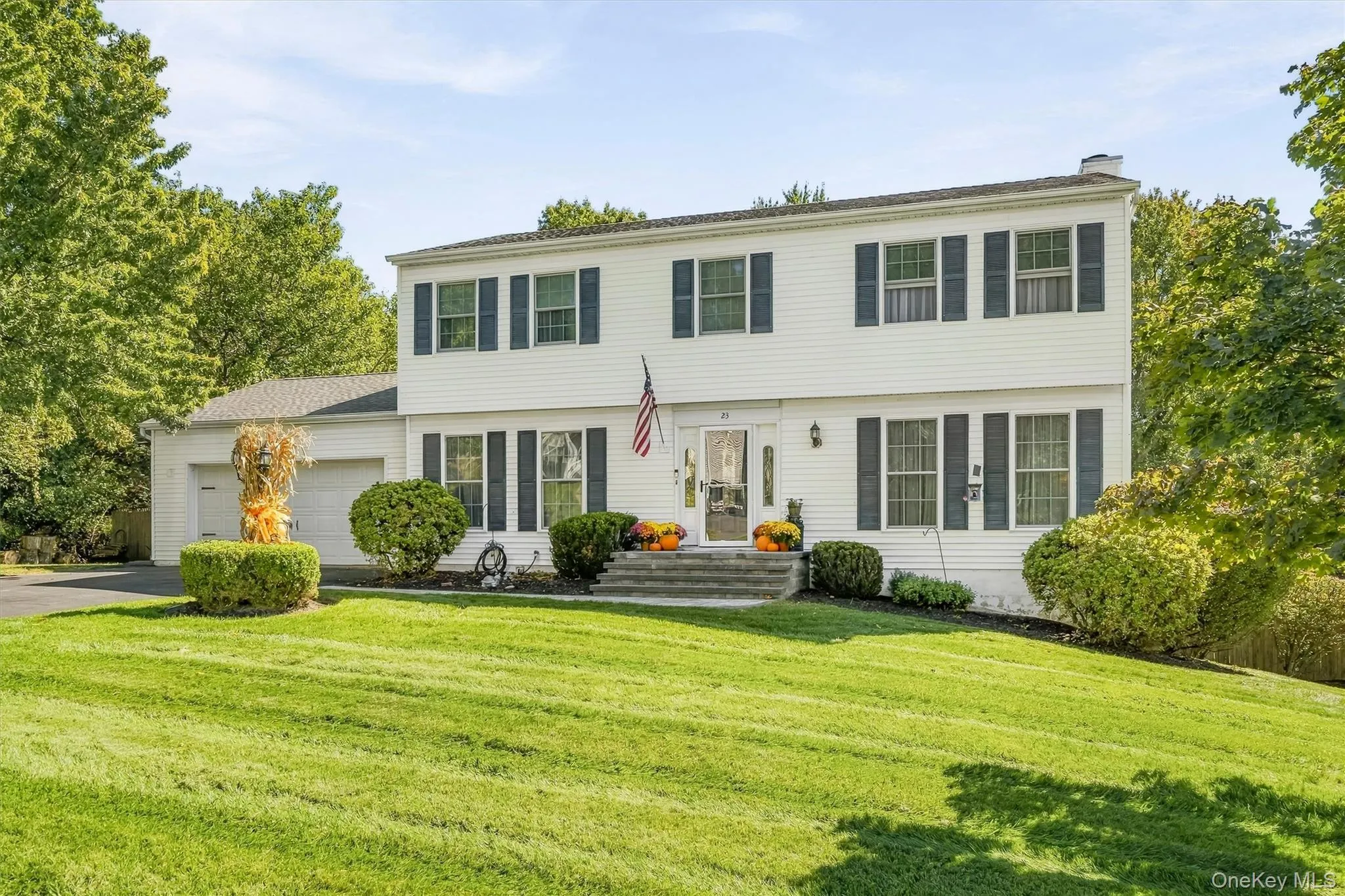 White siding exterior with dark shutters, attached two-car garage, established front landscaping, and a paved driveway White siding exterior with dark shutters, attached two-car garage, established front landscaping, and a paved driveway