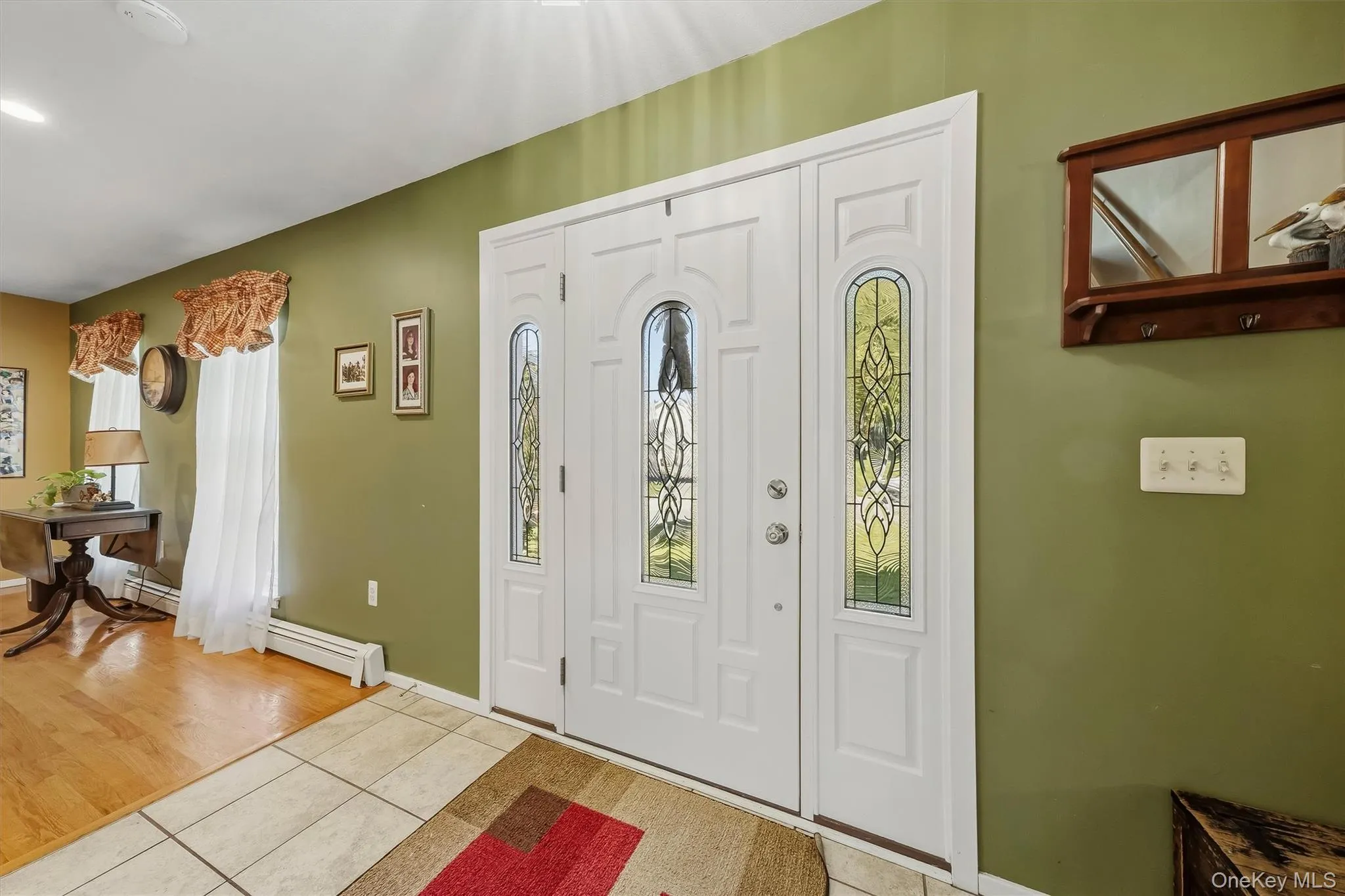Entryway featuring a white double door with decorative glass inserts, ceramic tile flooring, and wood-finish flooring Entryway featuring a white double door with decorative glass inserts, ceramic tile flooring, and wood-finish flooring