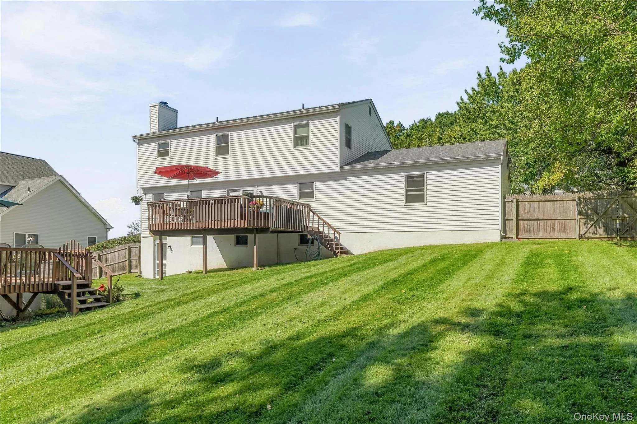 Expansive green lawn with a wood fence, two-story structure with siding, and a large wood deck with stairs Expansive green lawn with a wood fence, two-story structure with siding, and a large wood deck with stairs