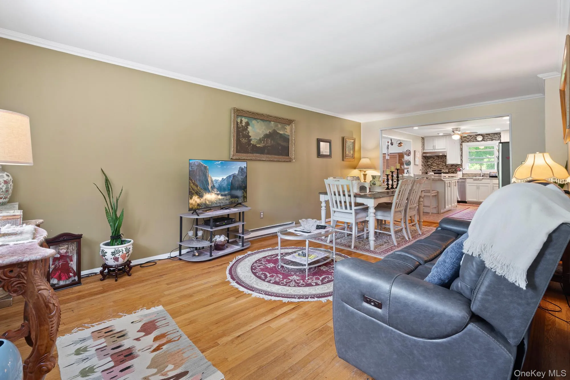 Living area with light wood-style floors, crown molding, baseboards, ceiling fan, and a baseboard radiator Living area with light wood-style floors, crown molding, baseboards, ceiling fan, and a baseboard radiator