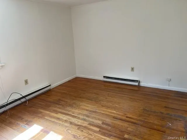 Spare room with baseboard heating, a baseboard heating unit, wood finished floors, baseboards, and ornamental molding Spare room with baseboard heating, a baseboard heating unit, wood finished floors, baseboards, and ornamental molding