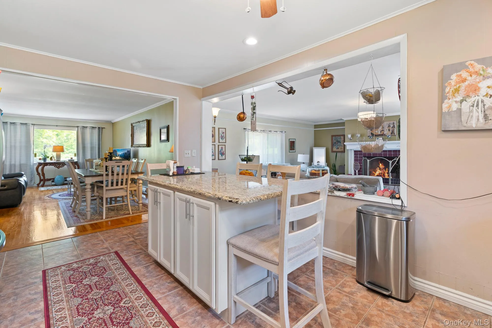 Kitchen with open floor plan, ornamental molding, white cabinets, a brick fireplace, and light stone counters Kitchen with open floor plan, ornamental molding, white cabinets, a brick fireplace, and light stone counters