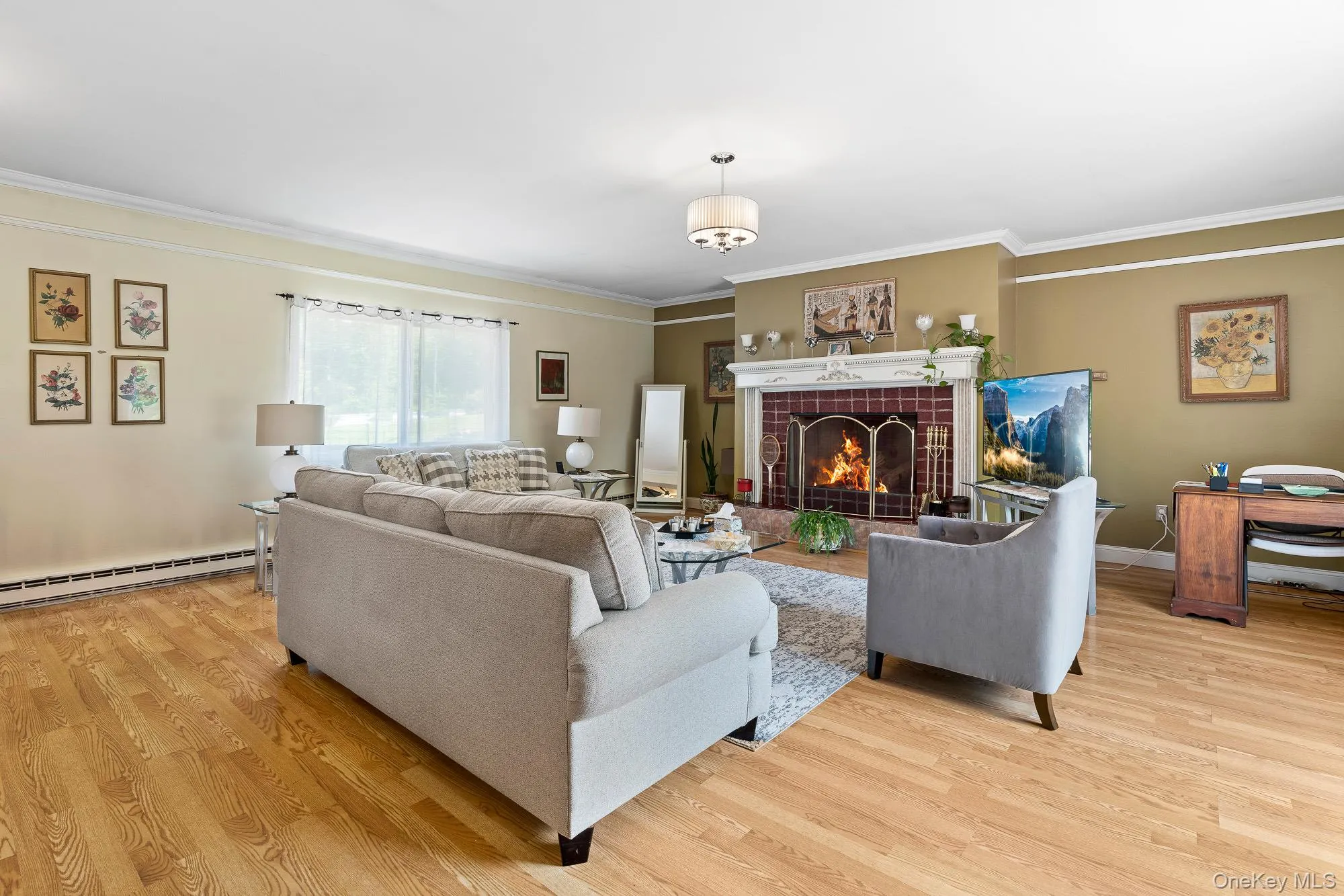 Living area with a baseboard heating unit, light wood-style floors, ornamental molding, a fireplace, and baseboards Living area with a baseboard heating unit, light wood-style floors, ornamental molding, a fireplace, and baseboards