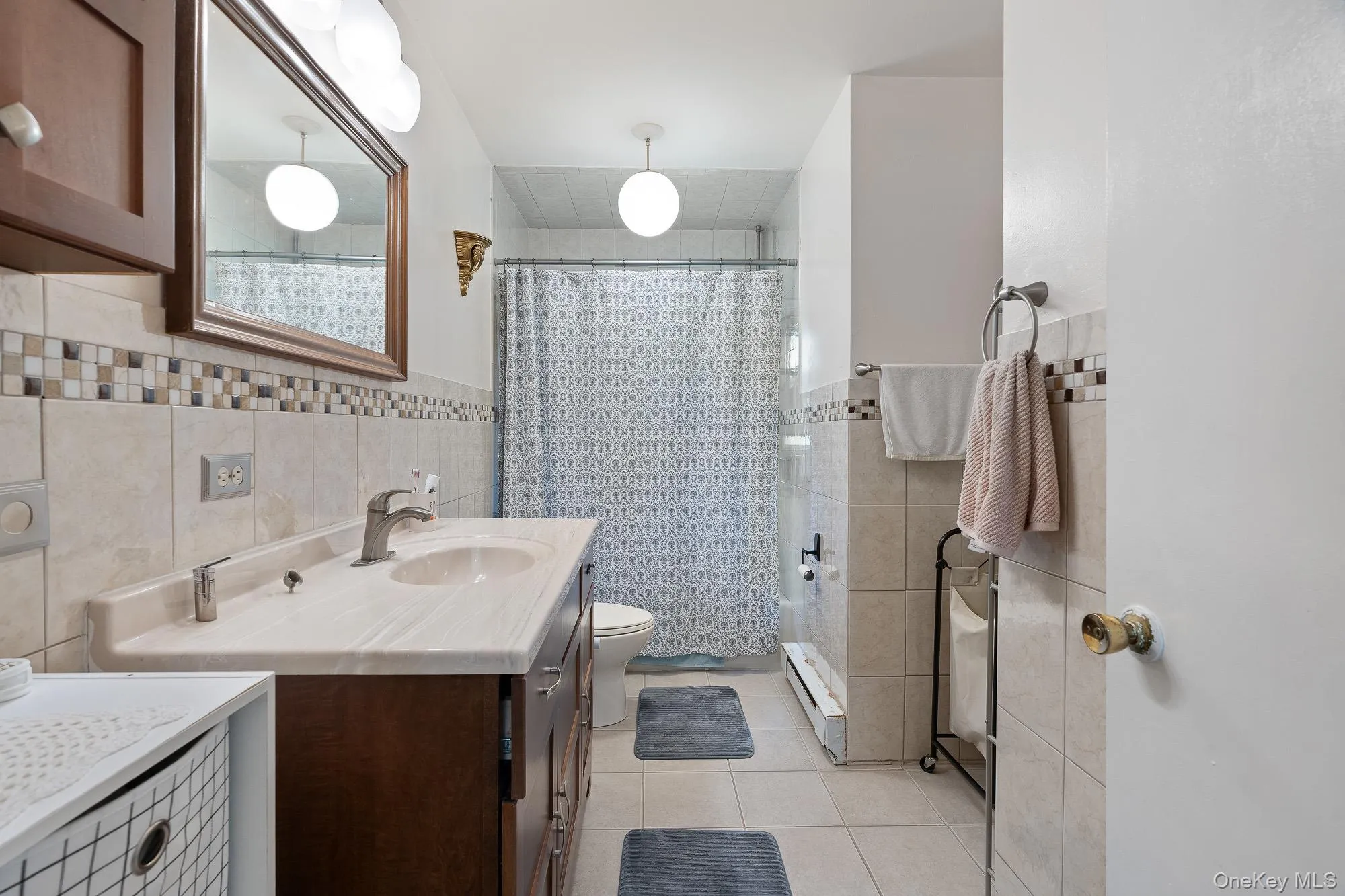 Bathroom with tile walls, vanity, tile patterned floors, toilet, and tiled shower Bathroom with tile walls, vanity, tile patterned floors, toilet, and tiled shower