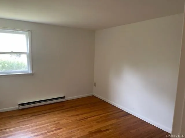 Spare room featuring a baseboard heating unit, wood finished floors, and baseboards Spare room featuring a baseboard heating unit, wood finished floors, and baseboards