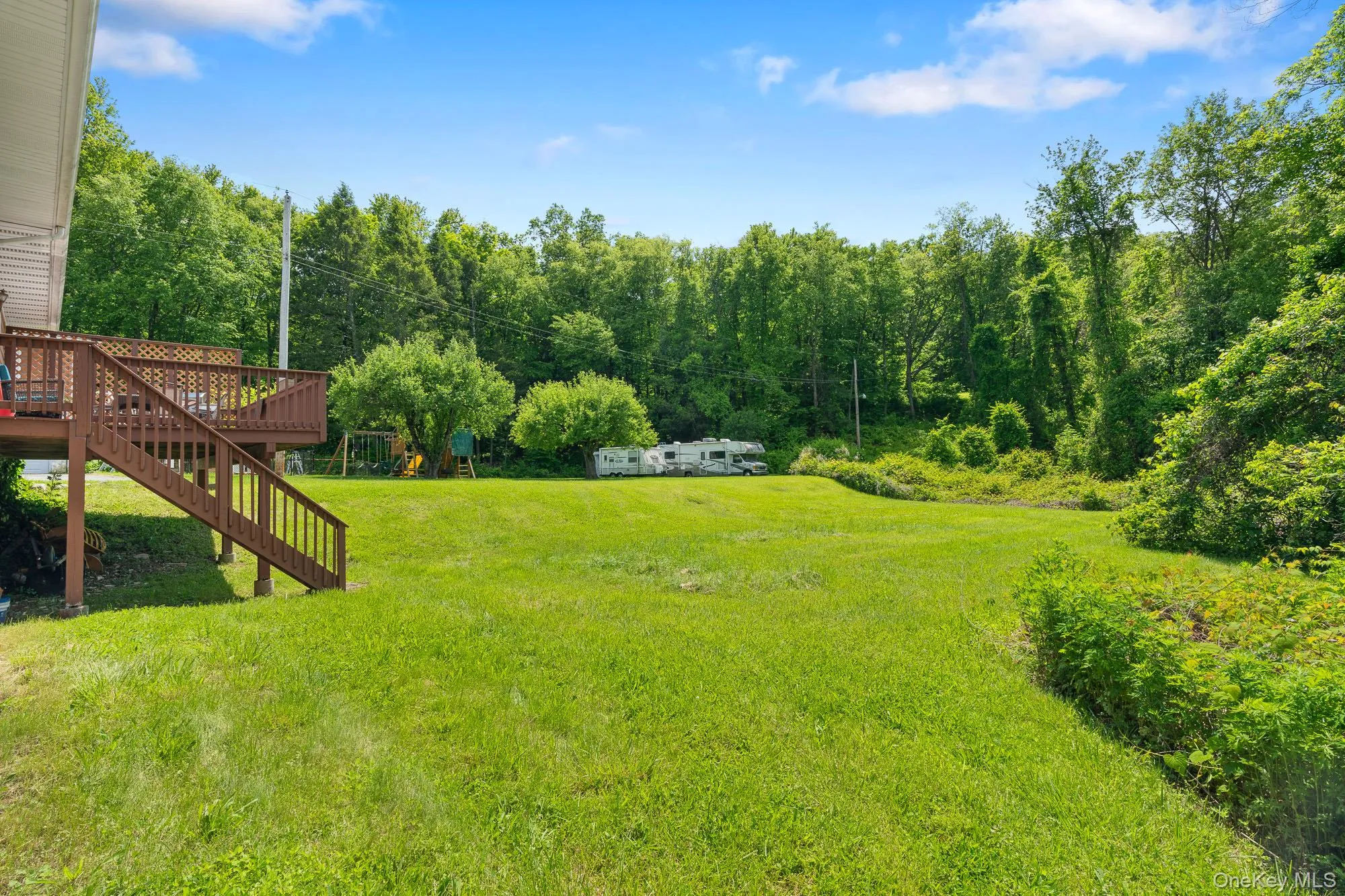View of grassy yard featuring a deck, stairway, and a wooded view View of grassy yard featuring a deck, stairway, and a wooded view