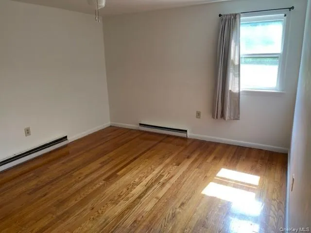 Empty room with a baseboard heating unit, wood finished floors, baseboards, and a ceiling fan Empty room with a baseboard heating unit, wood finished floors, baseboards, and a ceiling fan