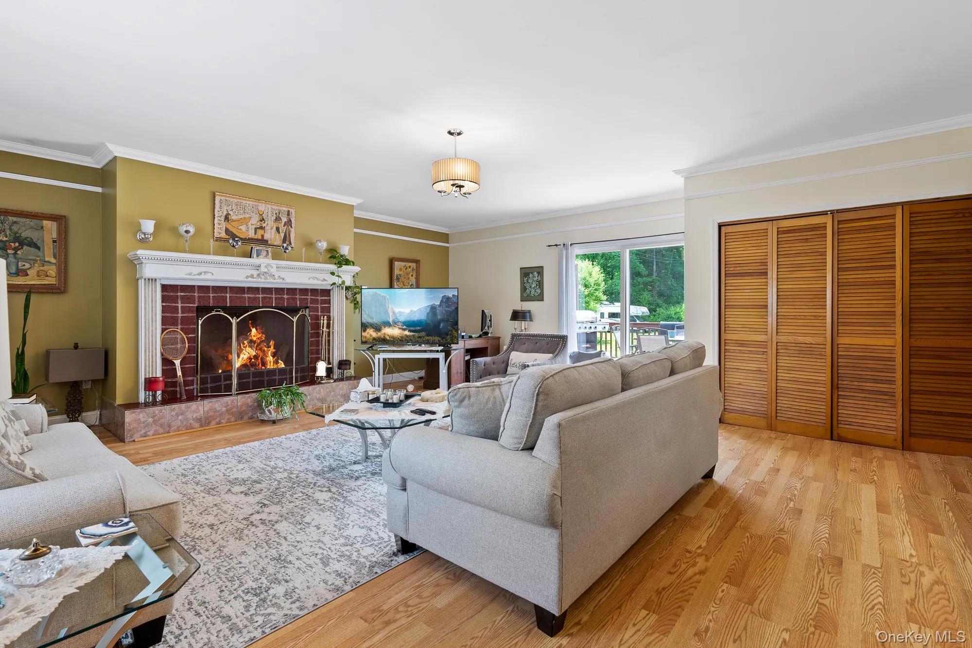 Living area featuring light wood finished floors, crown molding, and a tiled fireplace Living area featuring light wood finished floors, crown molding, and a tiled fireplace